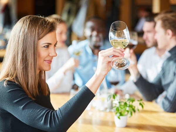 Mehrere Personen verkosten Wein. Im Vordergrund betrachtet eine Frau die Farbe des Weins im Glas.