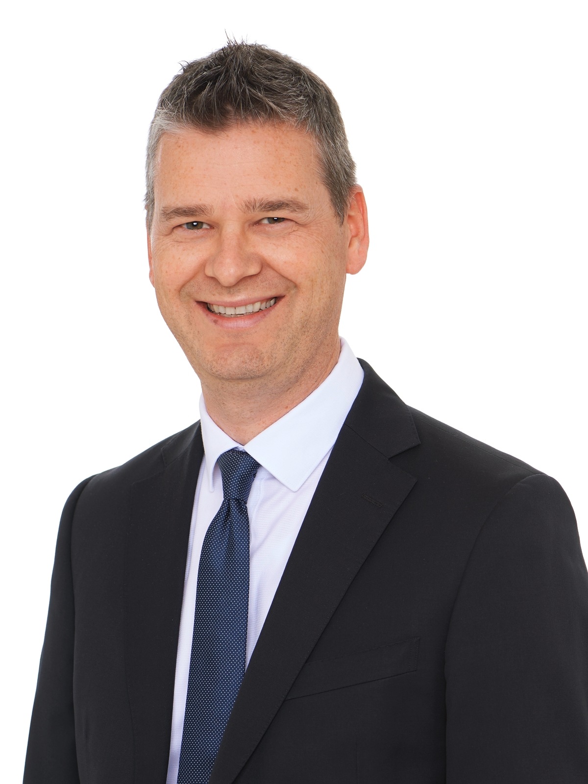 Portrait Christhard Deutscher. Lächelnder Mann mit weißem Hemd, schwarzem Jackett und Krawatte.