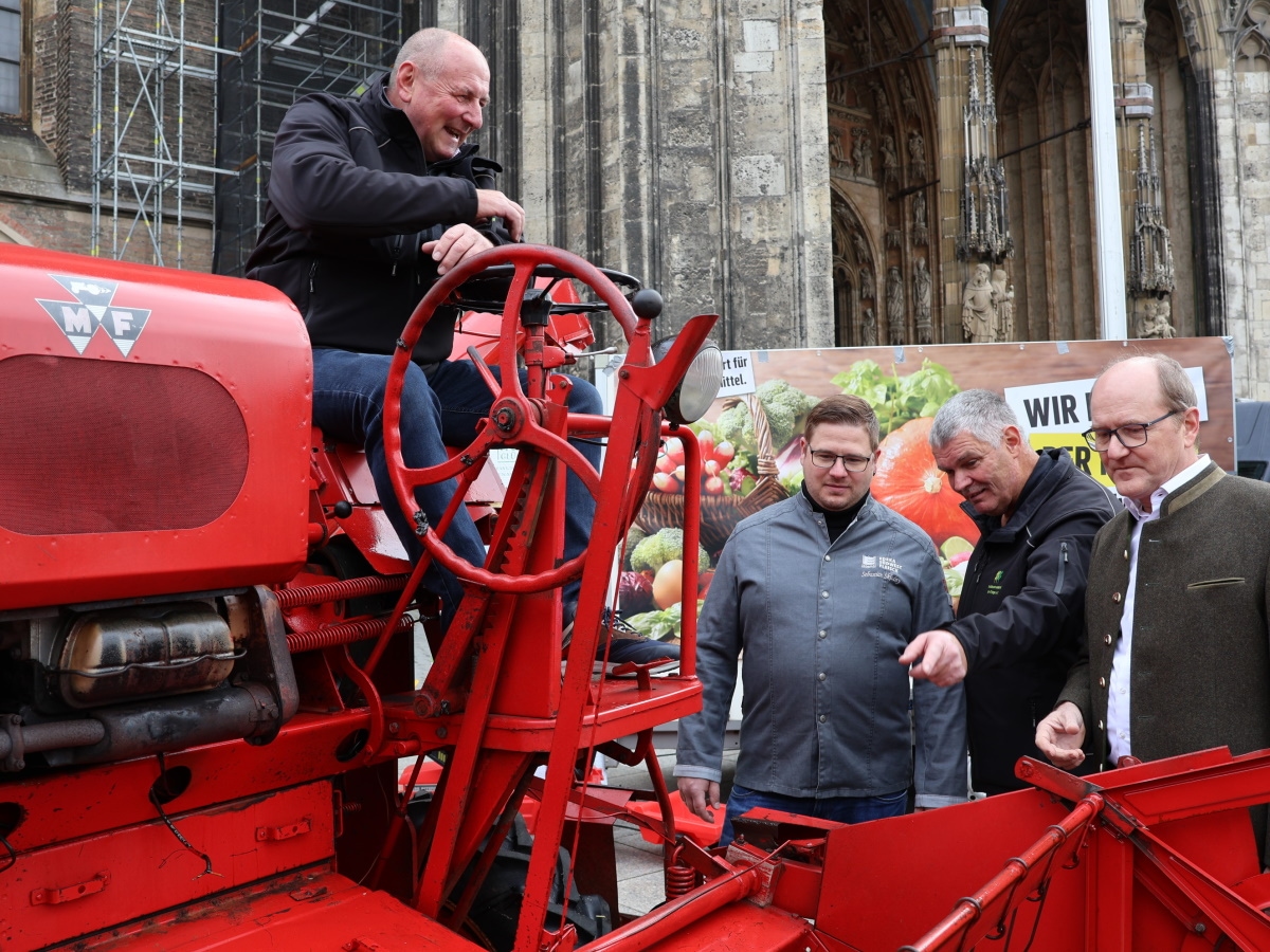 Ein Mann sitzt vor dem Ulmer Münster auf einer roten alten Landmaschine, drei Männer stehen daneben und schauen diese an