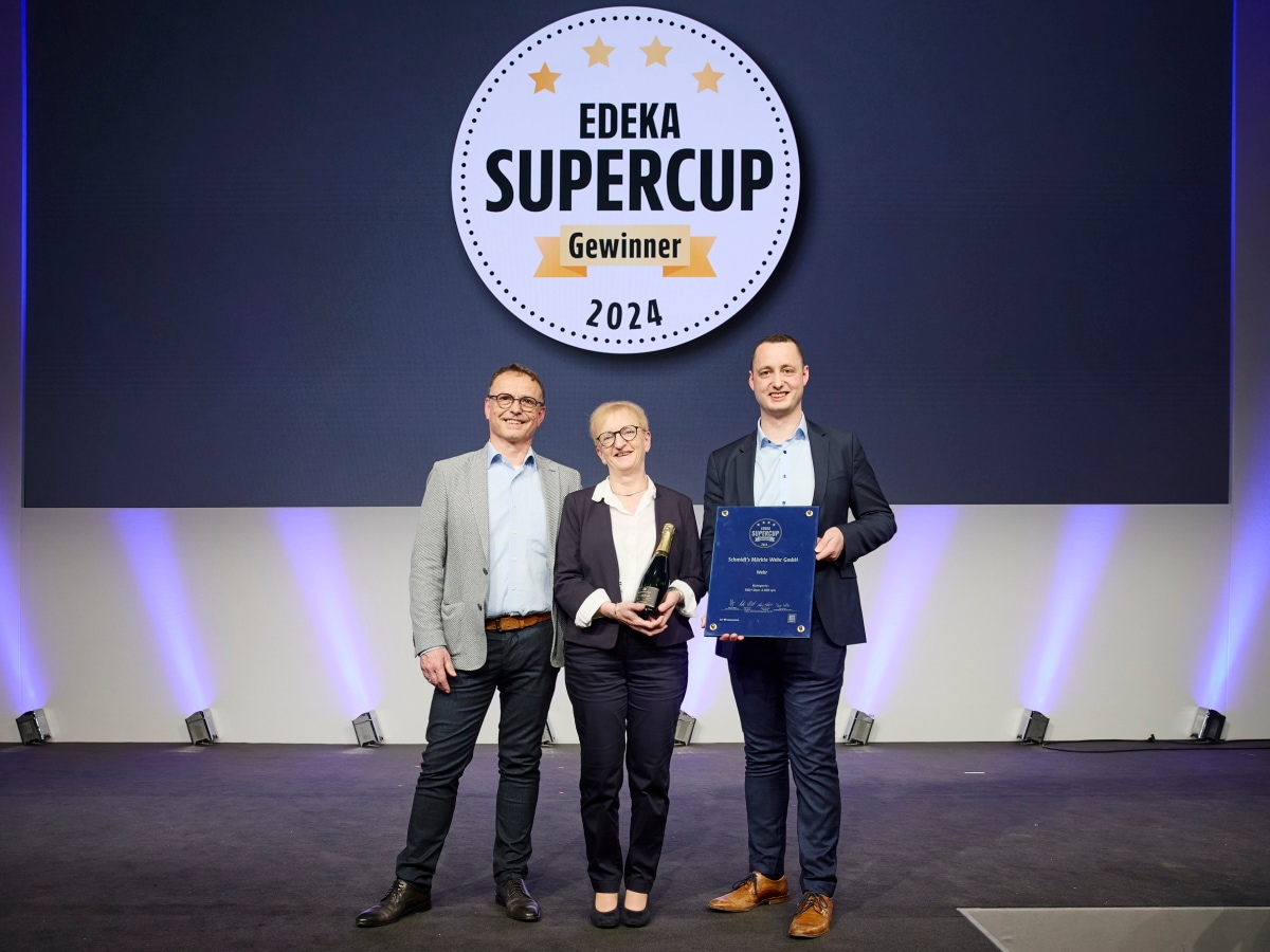 Eine Frau und zwei Männer zeigen ihre Sieger-Urkunde auf einer Bühne vor einer Leinwand mit dem Text  EDEKA Supercup Gewinner