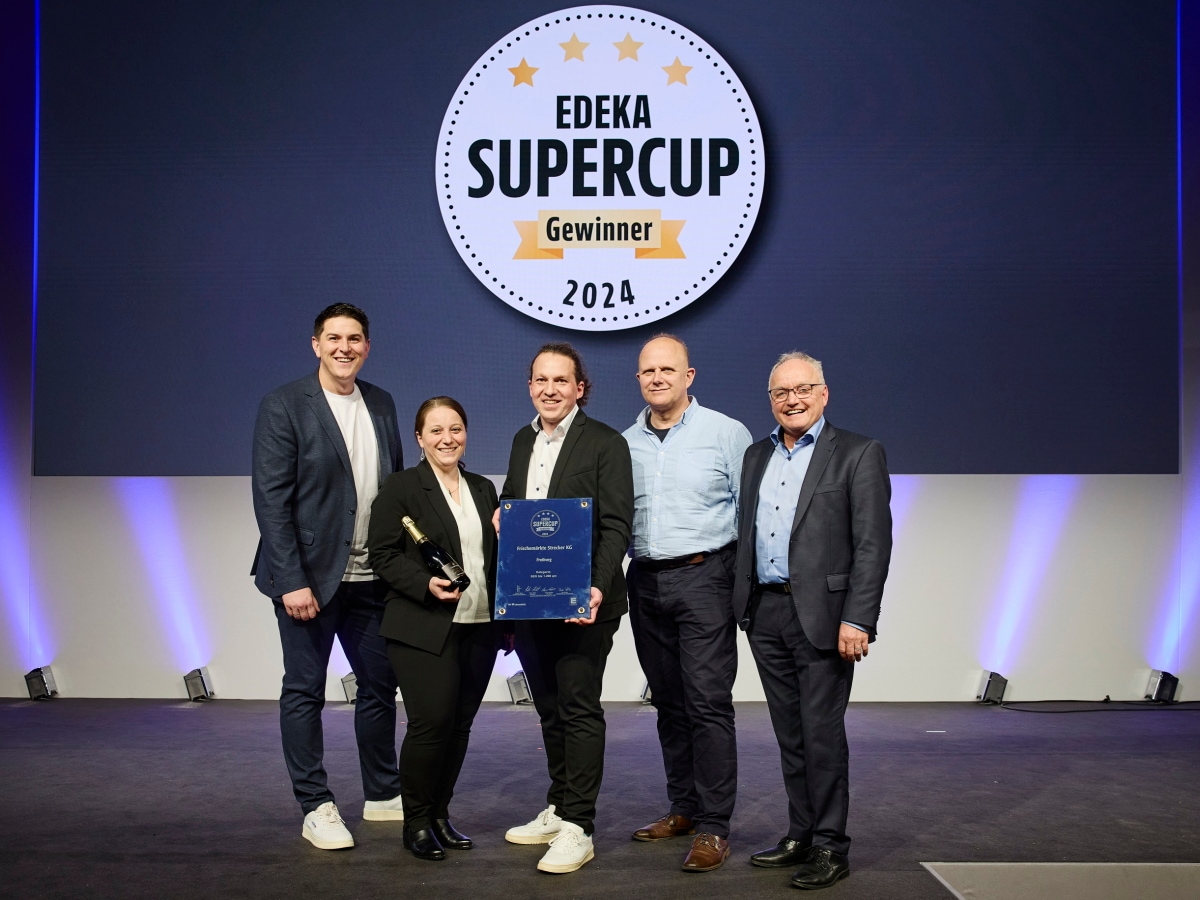 Vier Männer und eine Frau zeigen ihre Sieger-Urkunde auf einer Bühne vor einer Leinwand mit dem Text EDEKA Supercup Gewinner.