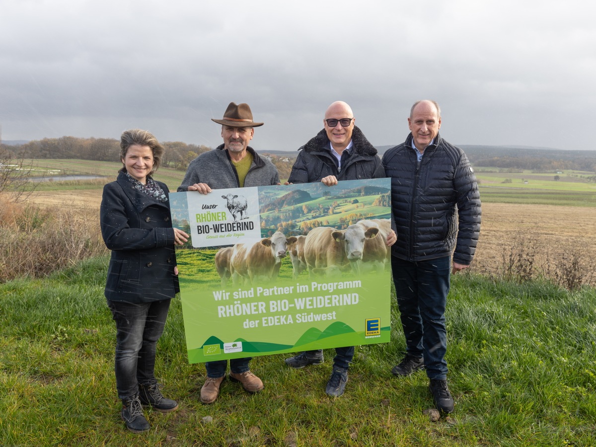 4 Personen stehen auf der Weide, graue Wolken, Wind, und halten ein Schild mit Rhöner Bio-Weiderind Partner der EDEKA Südwest