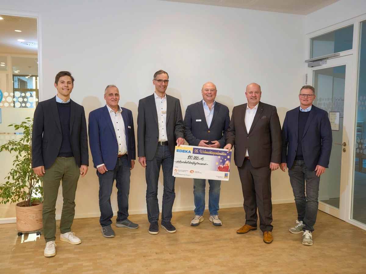 6 Männer stehen nebeneinander, alle in Jackets. 2 halten einen symbolischen Scheck mit Text: EDEKA Weihnachtspendenaktion