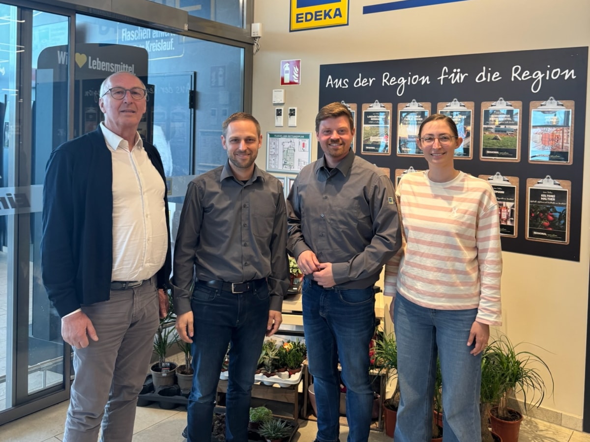 Lächelnder Landtagsabgeordneter steht zusammen mit 3 Personen der Kaufmannsfamilie im Eingangsbereich des EDEKA-Marktes.