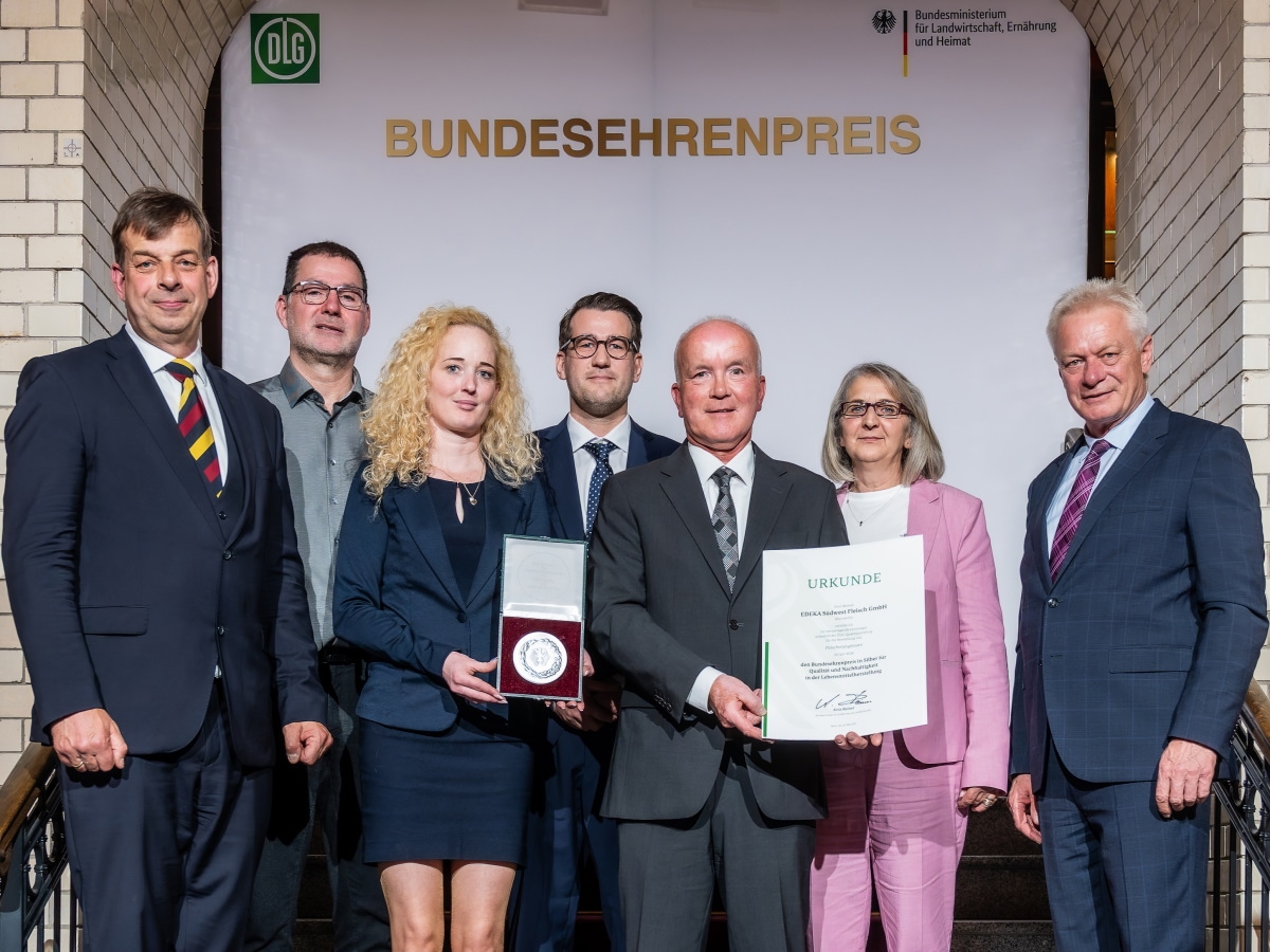 7 Personen stehen mit der Urkunde und Medaille auf einer Treppe