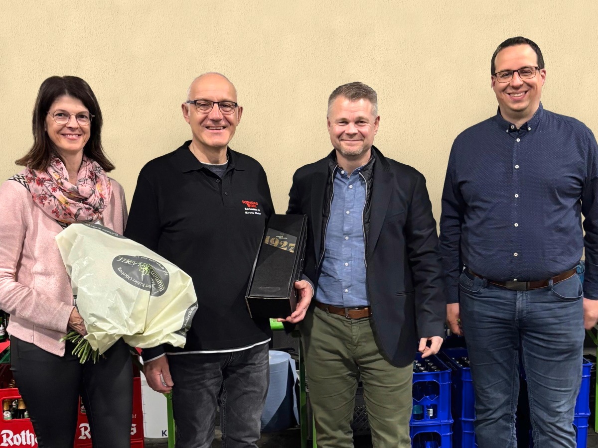 Eine Frau mit Blumenstrauß und 3 Männer stehen vor Getränkekisten.