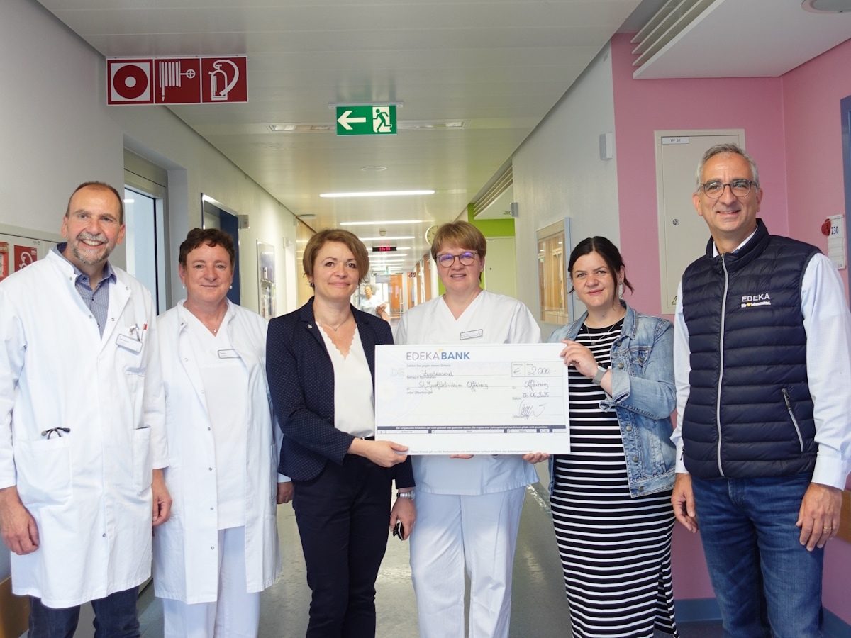 6 Personen stehen im Flur einer Krankenstation und halten einen symolischen Spendenscheck.
