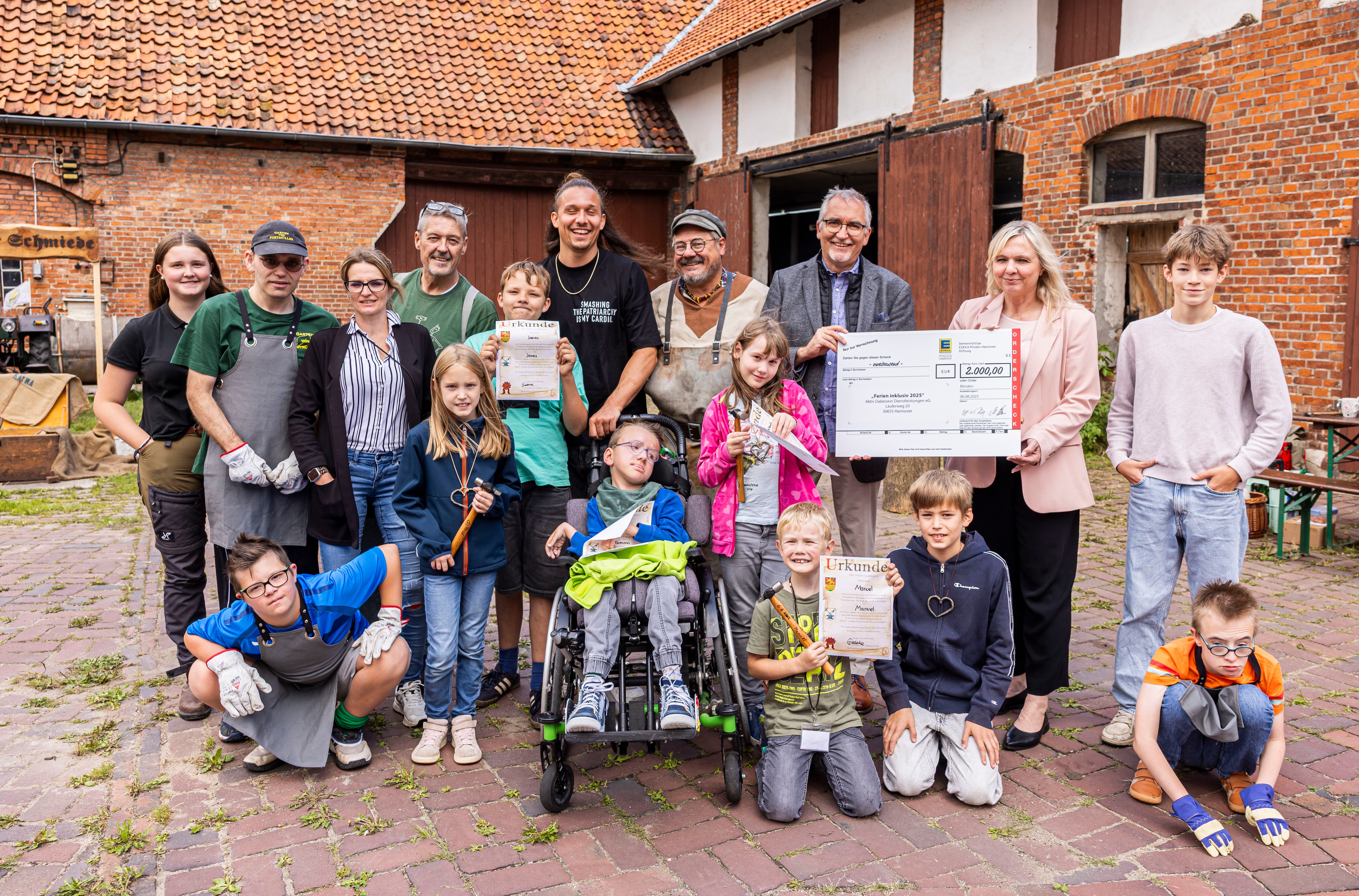 Eine Gruppe von Kindern, Jugendlichen, ihre Betreuer und EDEKA-Vertreter stehen mit dem Spendenscheck vor einer Scheune.