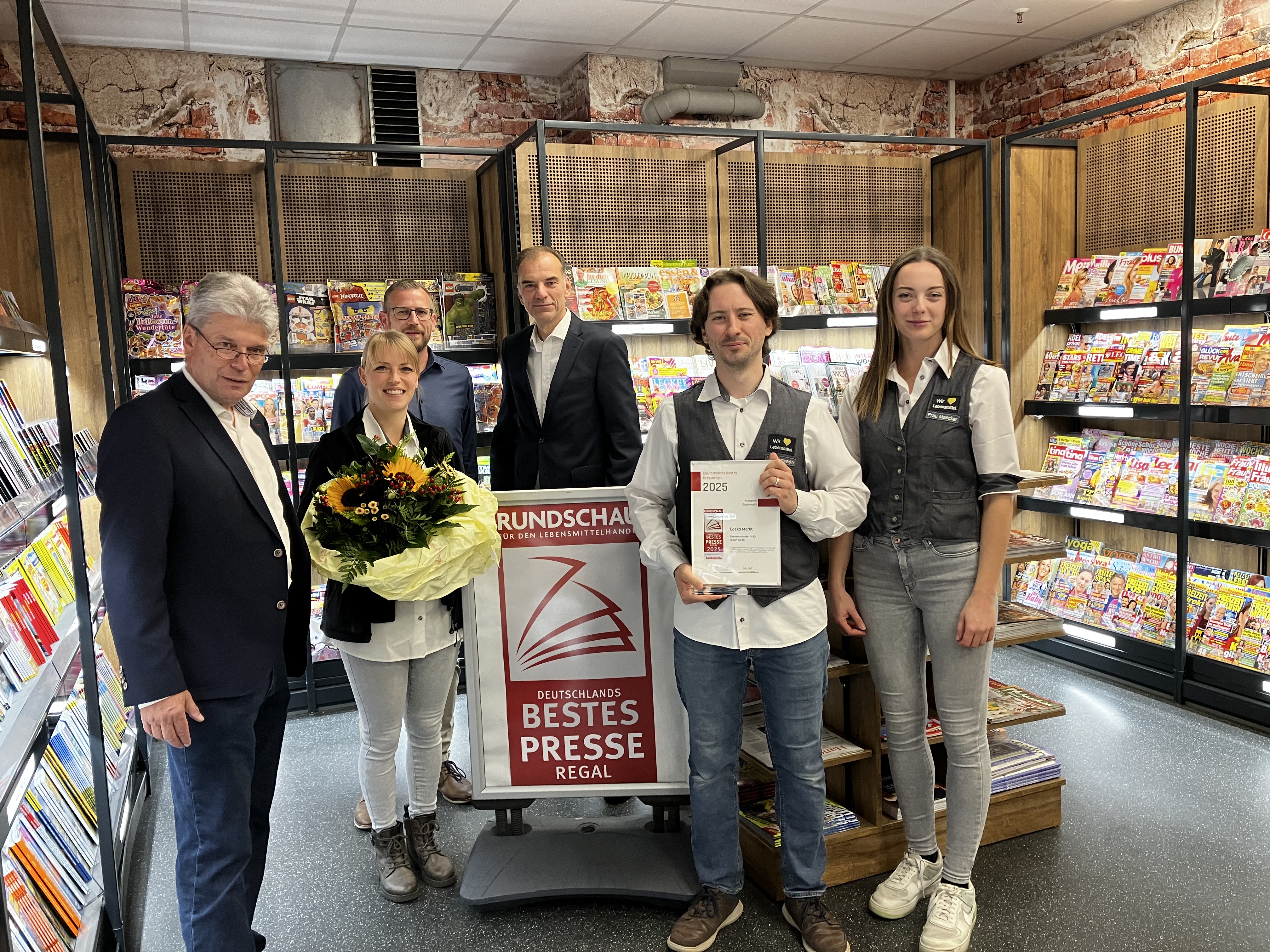 Die Trophäe zu "Deutschlands besten Presseregal" wird in der Zeitschriftenabteilung des EDEKA Siemensstraße übergeben.