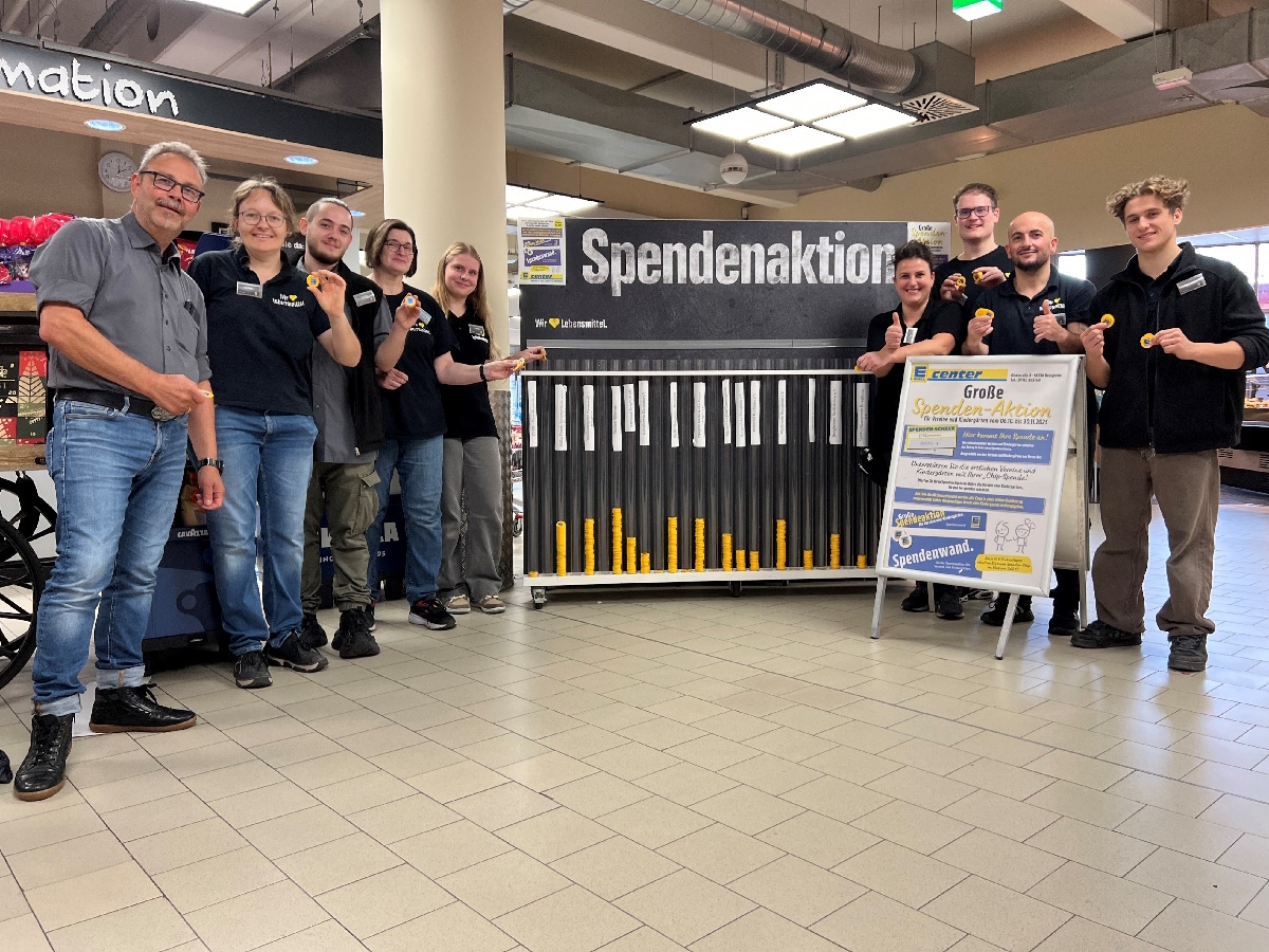 9 MItarbeitende des E centers stehen vor einer Spendenwand im Marktfoyer