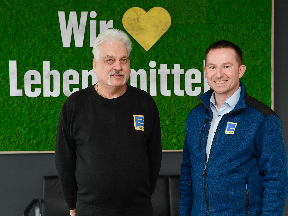 2 Männer stehen vor einer Wand mit "Wir lieben Lebensmittel" 
