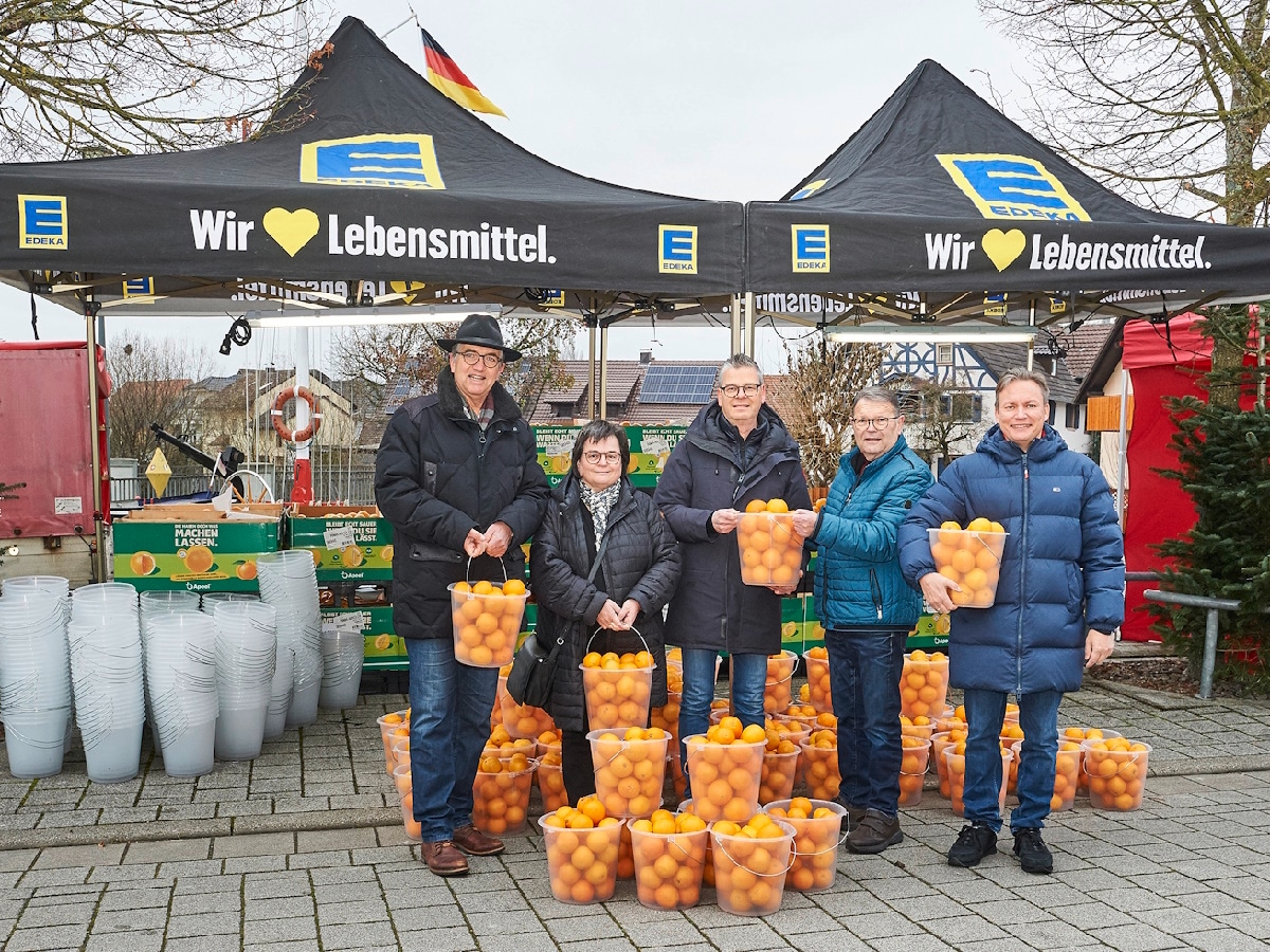 5 Personen stehen mit Orangen-Eimer vor EDEKA-Zeltständen
