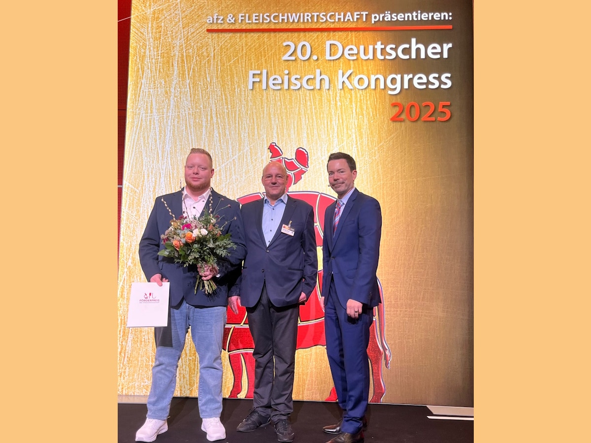 Drei Männer stehen auf der Bühne, Nikolas Imorde hält eine Urkunde und einen Blumenstrauß in den Händen. 