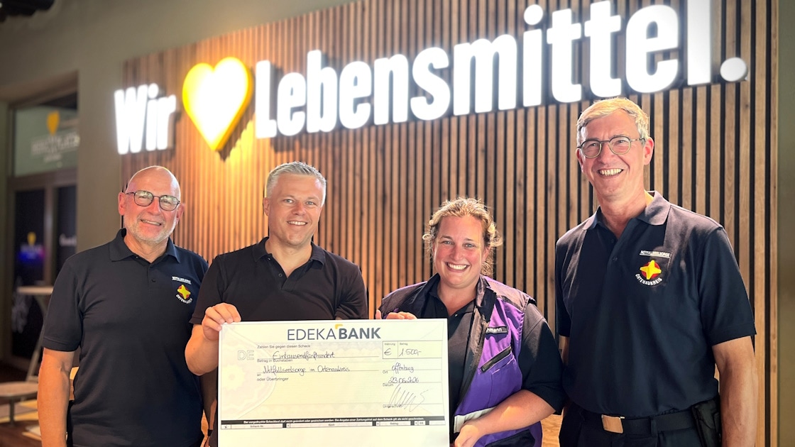 3 Männer und 1 Frau stehen mit einem symbolischen Spendenscheck vor einer Holzwand mit "Wir lieben Lebensmittel"