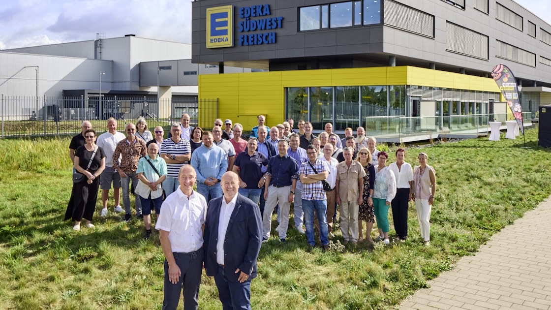 Eine große Gruppe Menschen steht auf dem Rasen vor dem EDEKA Südwest Fleisch Gebäude.