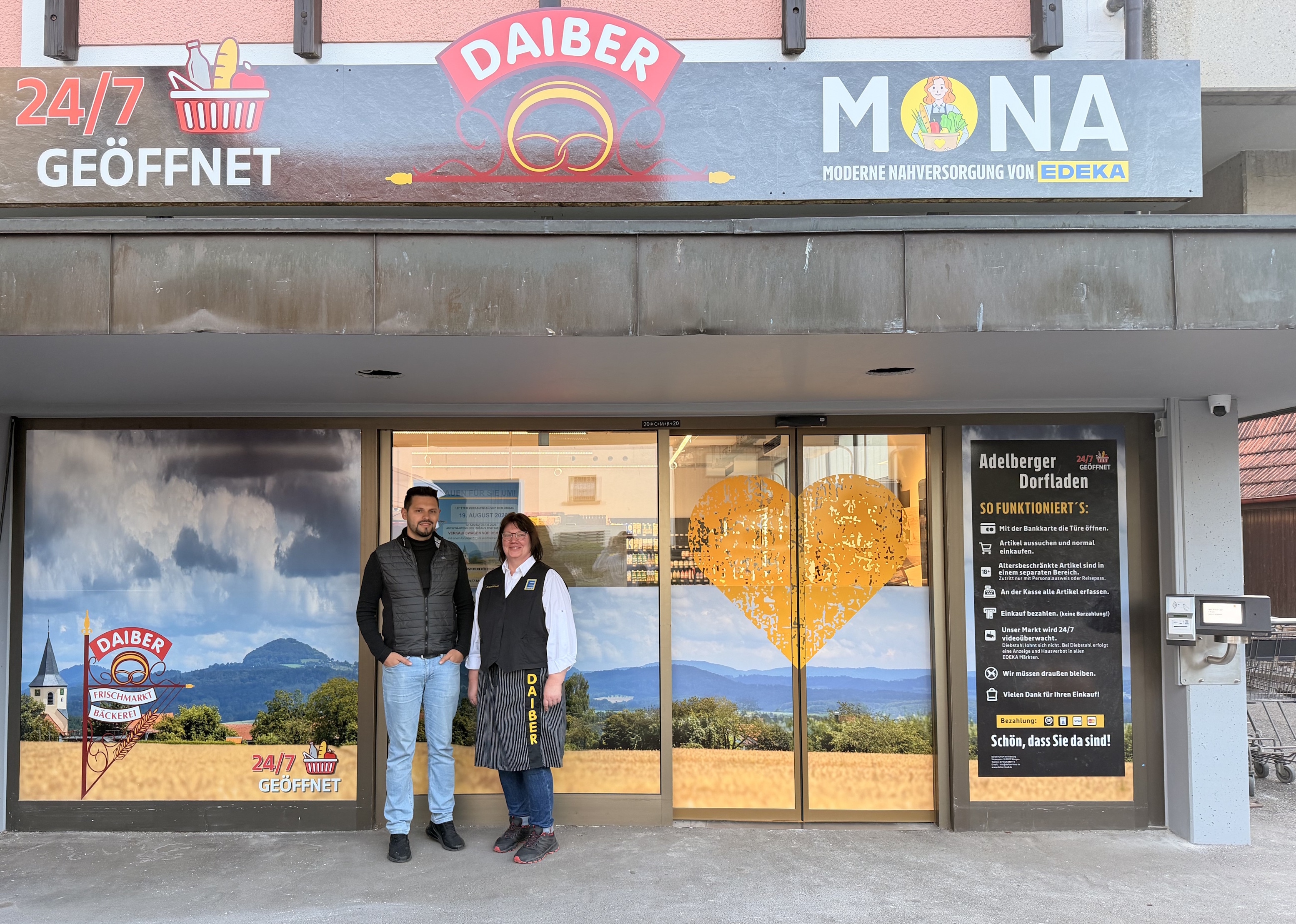 Ein Mann und eine Frau stehen vor dem eines kleinen Marktes, darüber hängt eine Schild 24/7 geöffnet, Daiber und MONA (Moderne Nahversorgung von EDEKA)