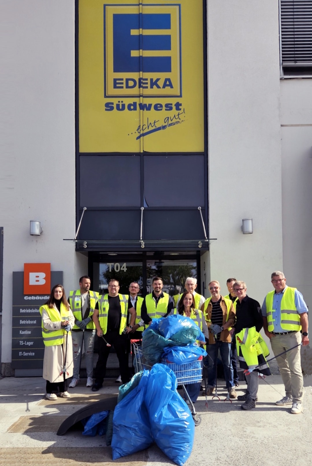 11 Mitarbeitende mit gelben Warnwesten, Müllzangen und gefüllten Müllsäcken stehen vor dem EDEKA Südwest Gebäude