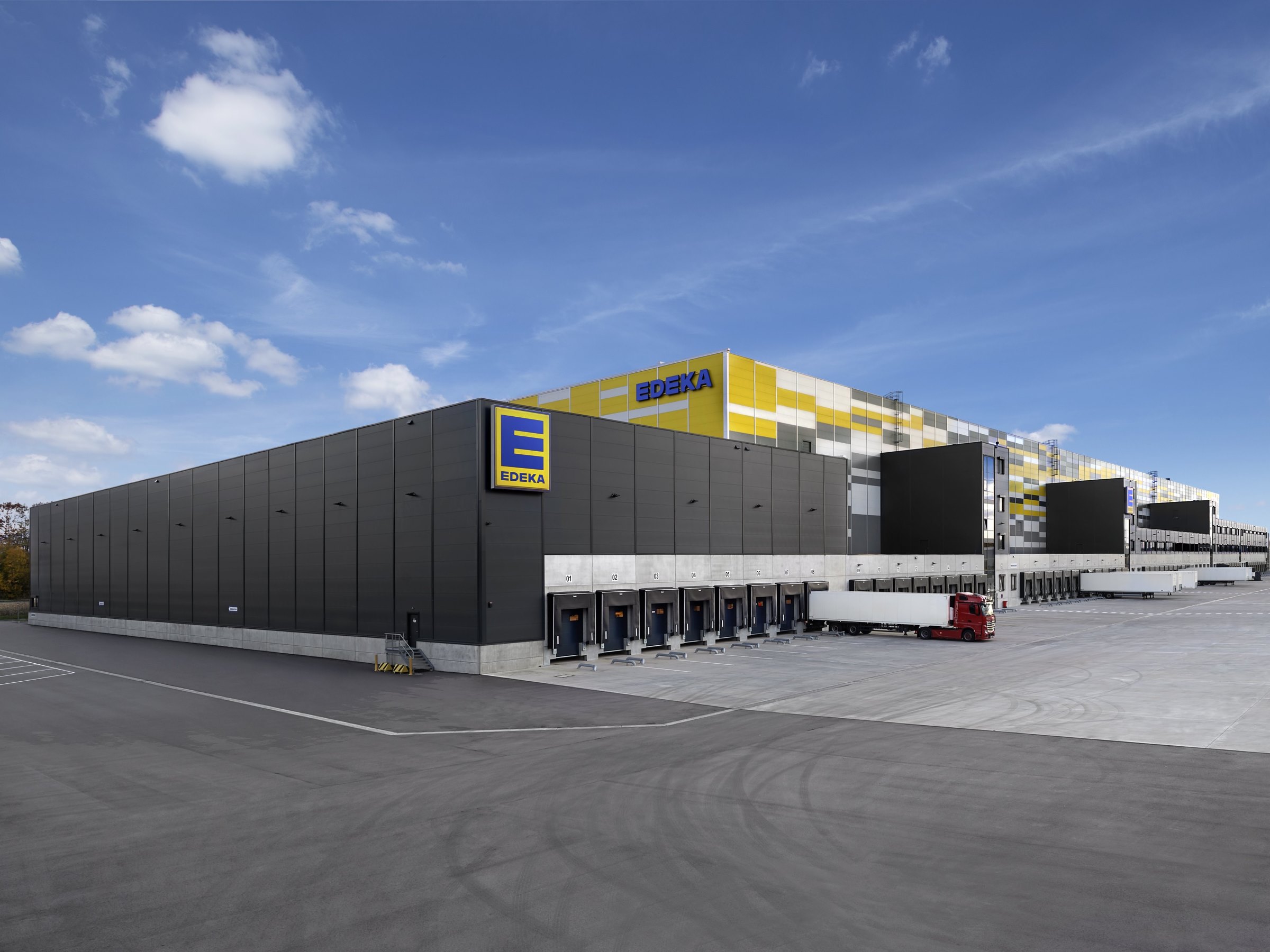 Langes modernes Logistikgebäude mit EDEKA Schriftzug und zahlreichen Toren für zum Be- und entladen von Lkws