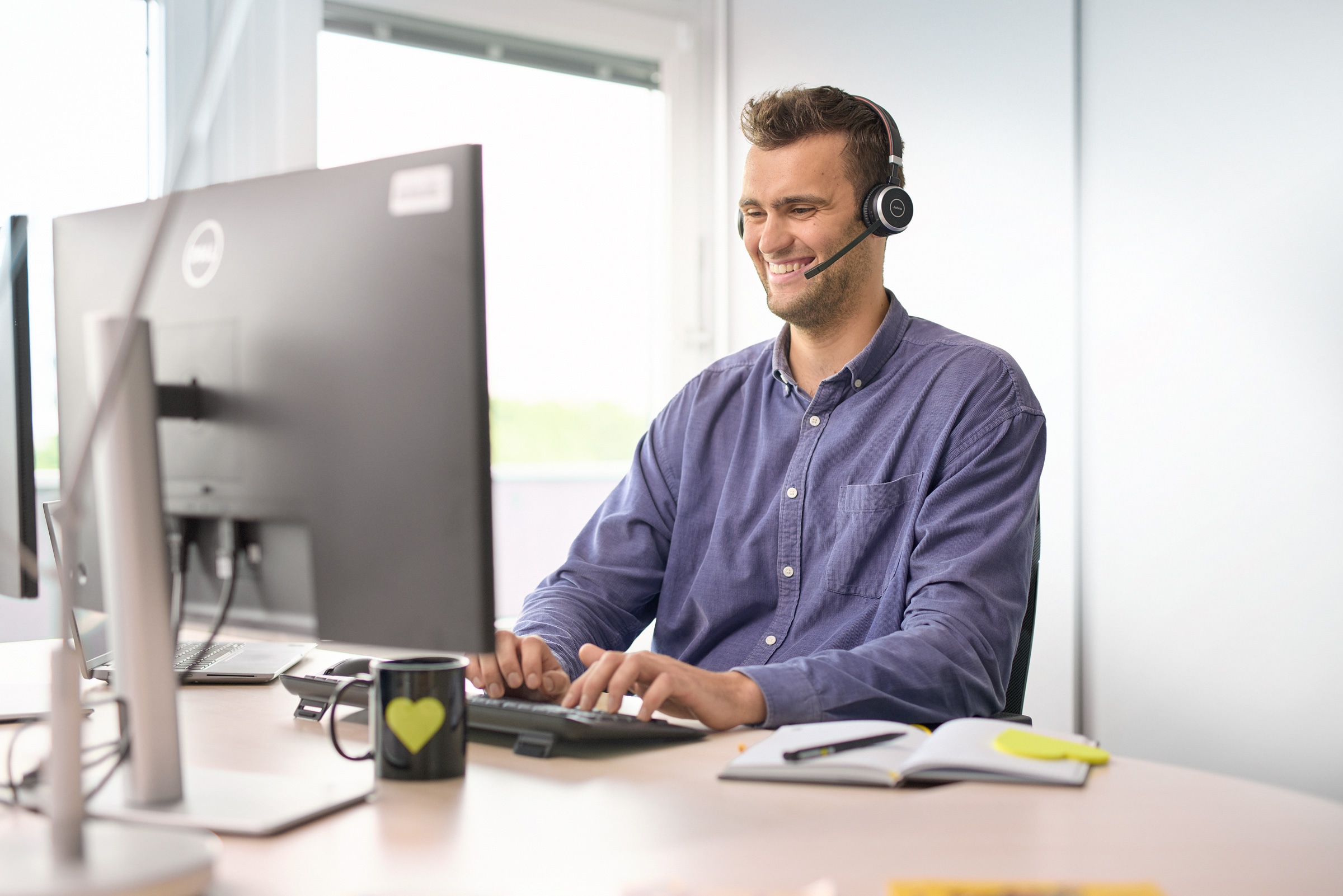 Junger Mann sitzt lächelnd vor seinem Computer