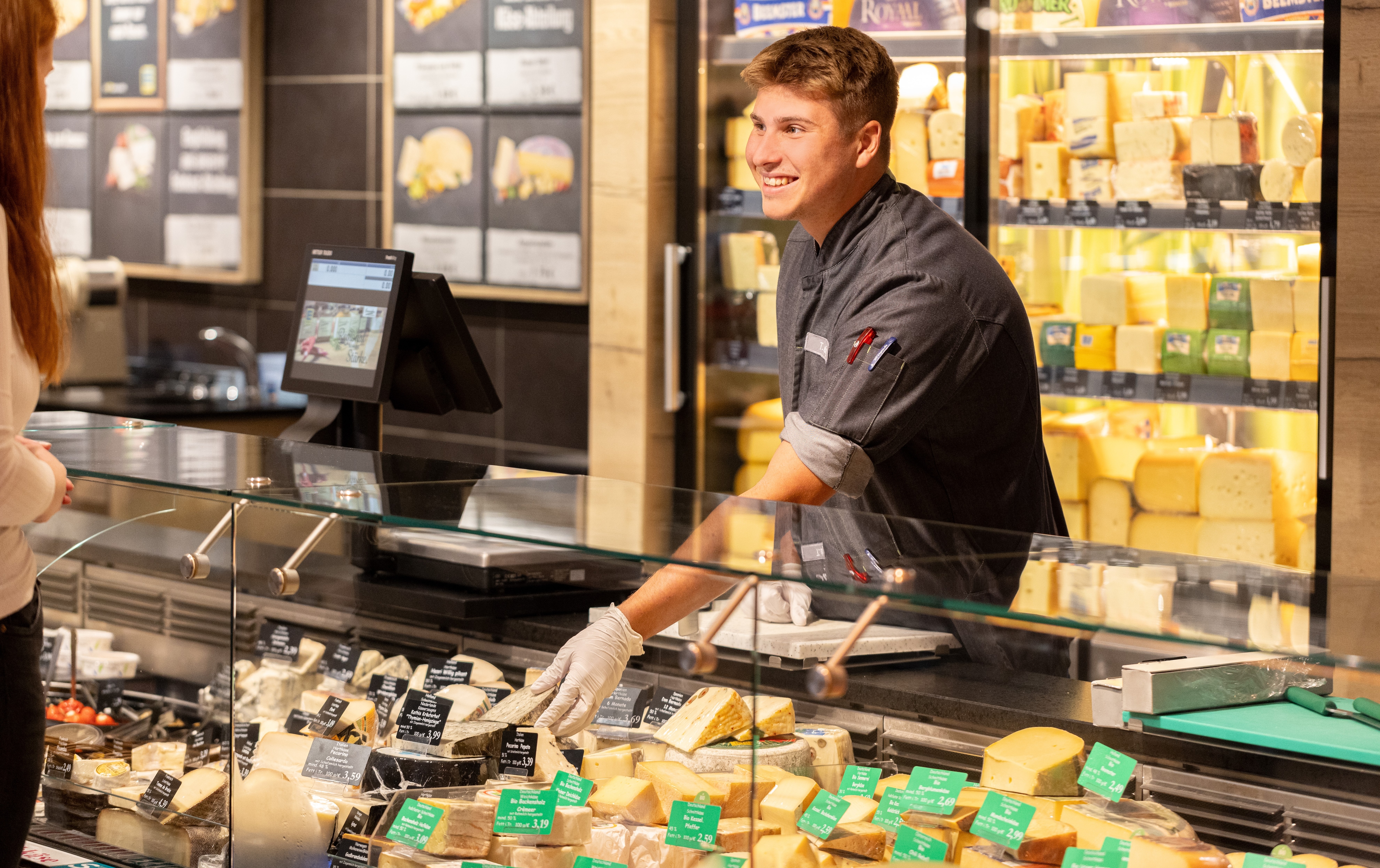 Junger lachender Mann hinter der Käsetheke eines EDEKA-Marktes.