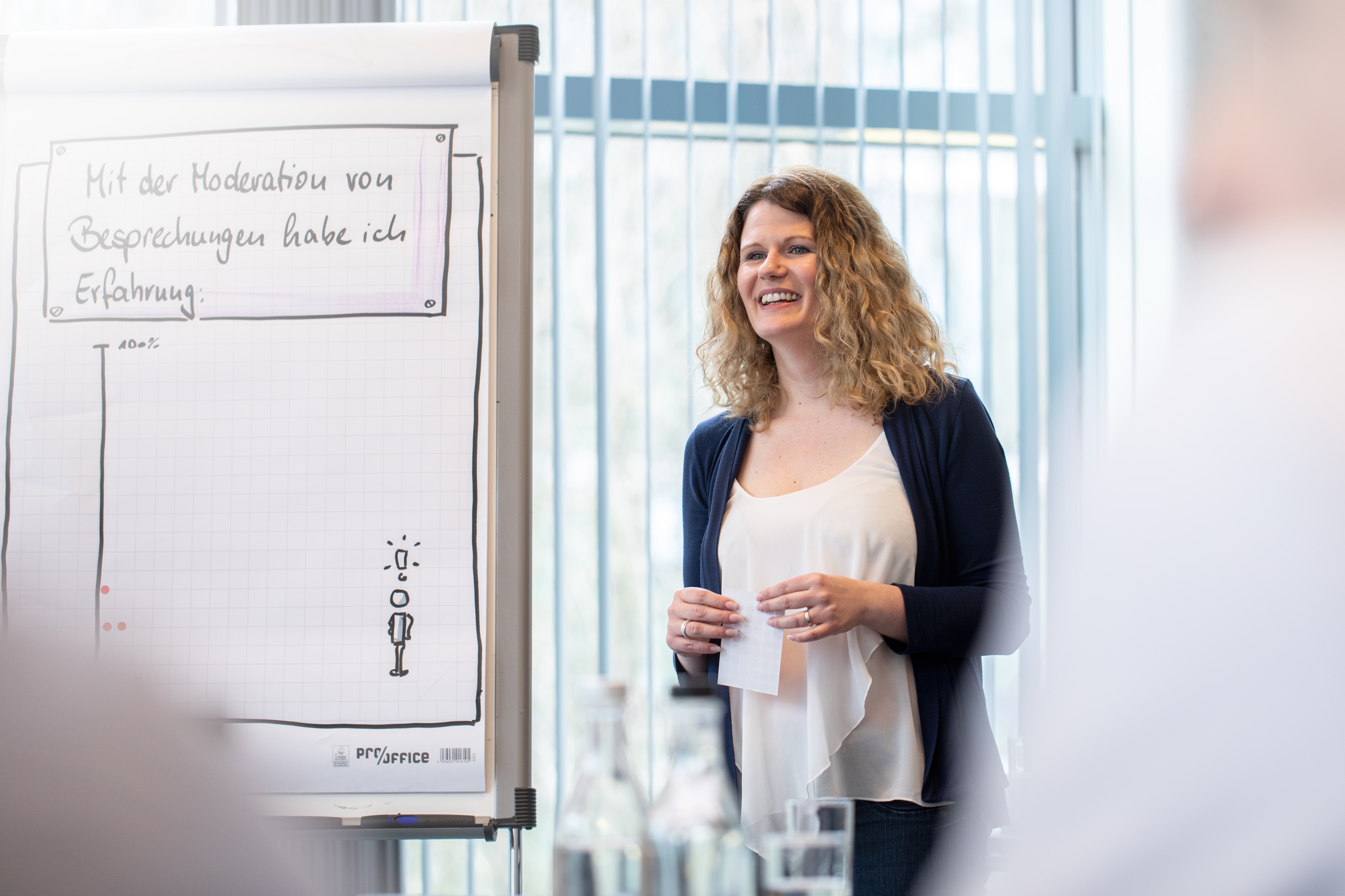 Junge Frau steht neben einem Flipchart und präsentiert während eines Seminars.