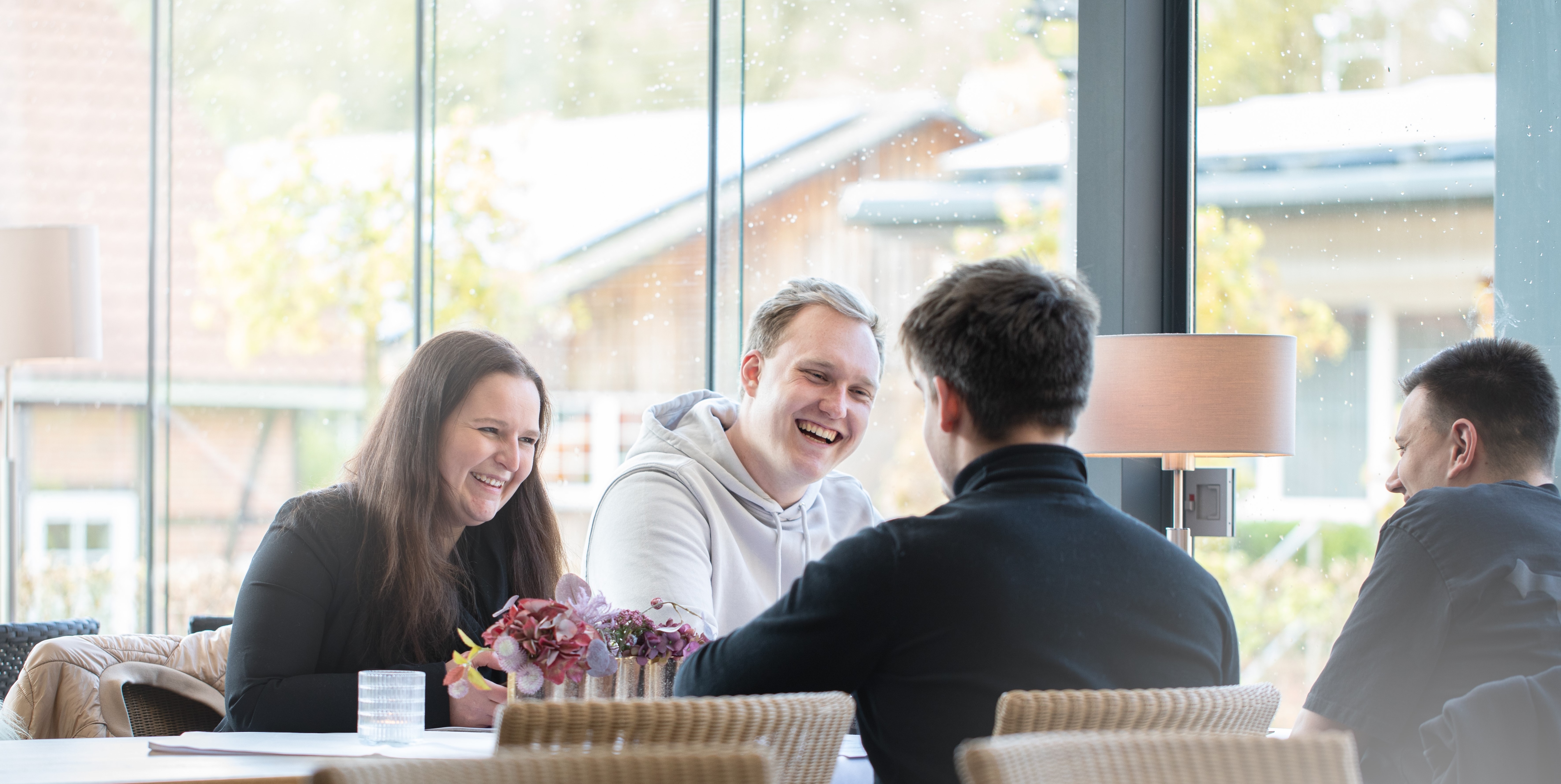 Junge Personen sitzen während eines Seminars am Tisch und lachen.