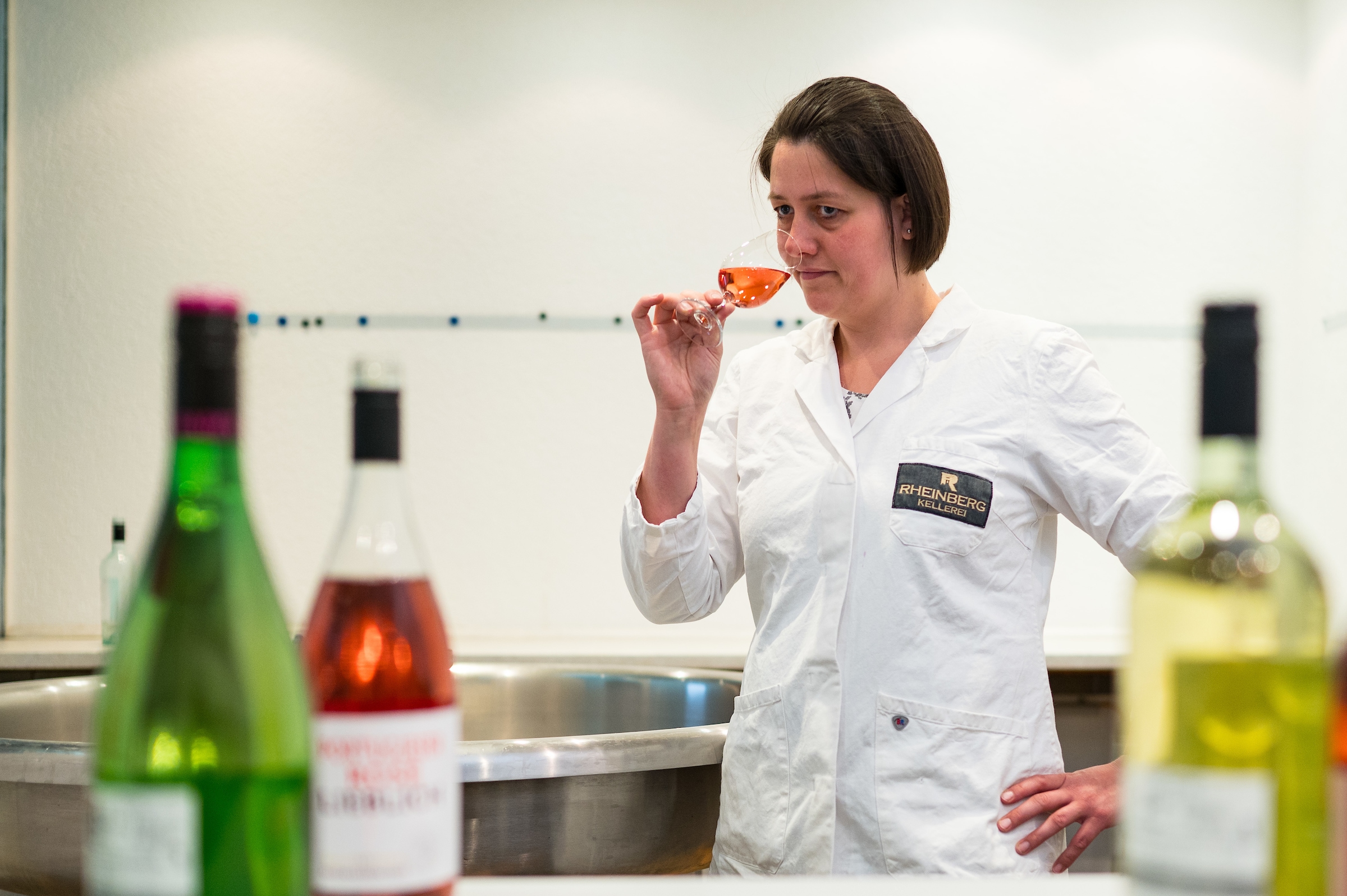 Labor-Mitarbeiterin riecht an einem Glas Wein, im Vordergrund stehen Flaschen 