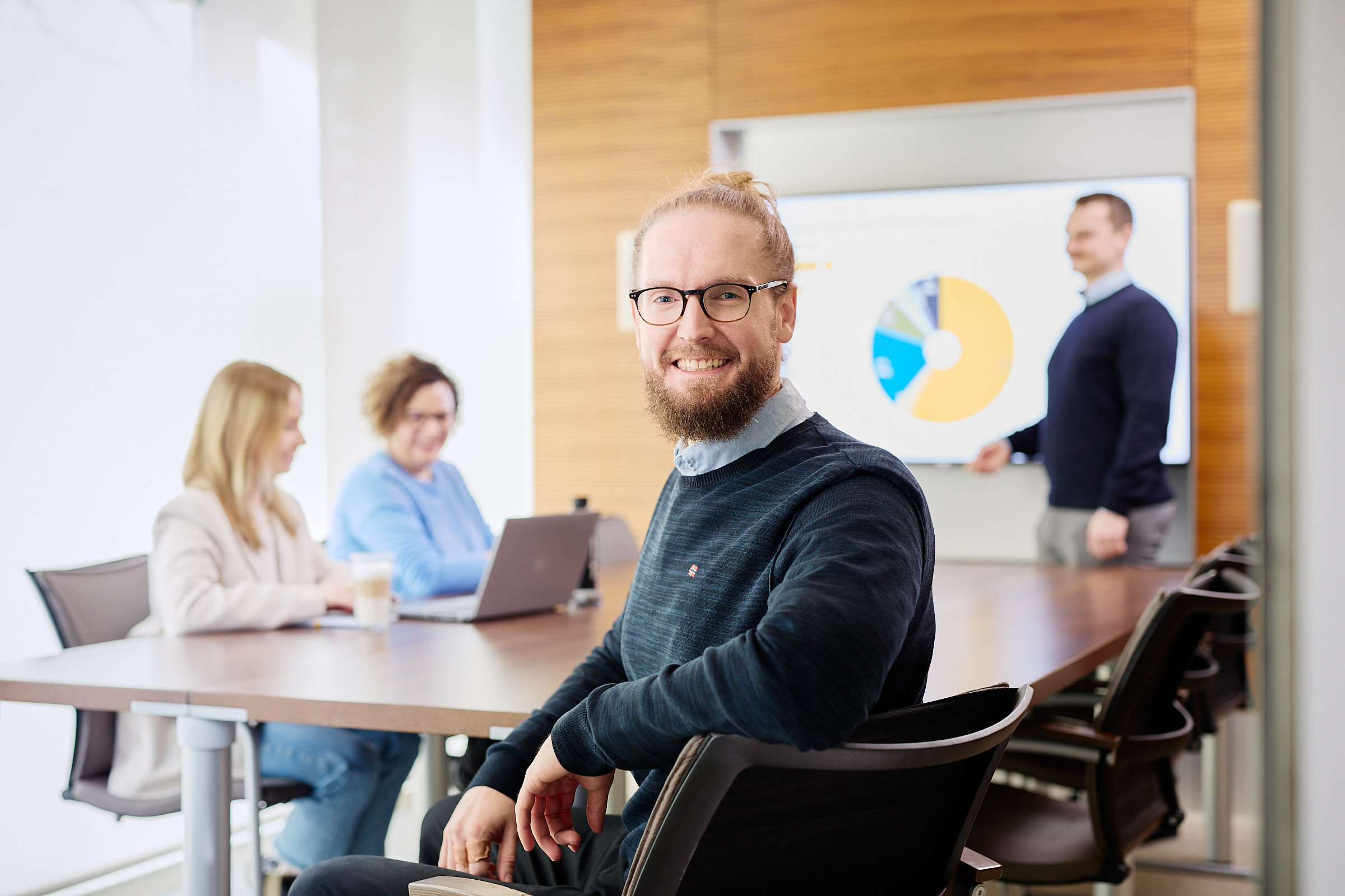 Mitarbeiter im Meeting schaut über die Schulter lächelnd in die Kamera