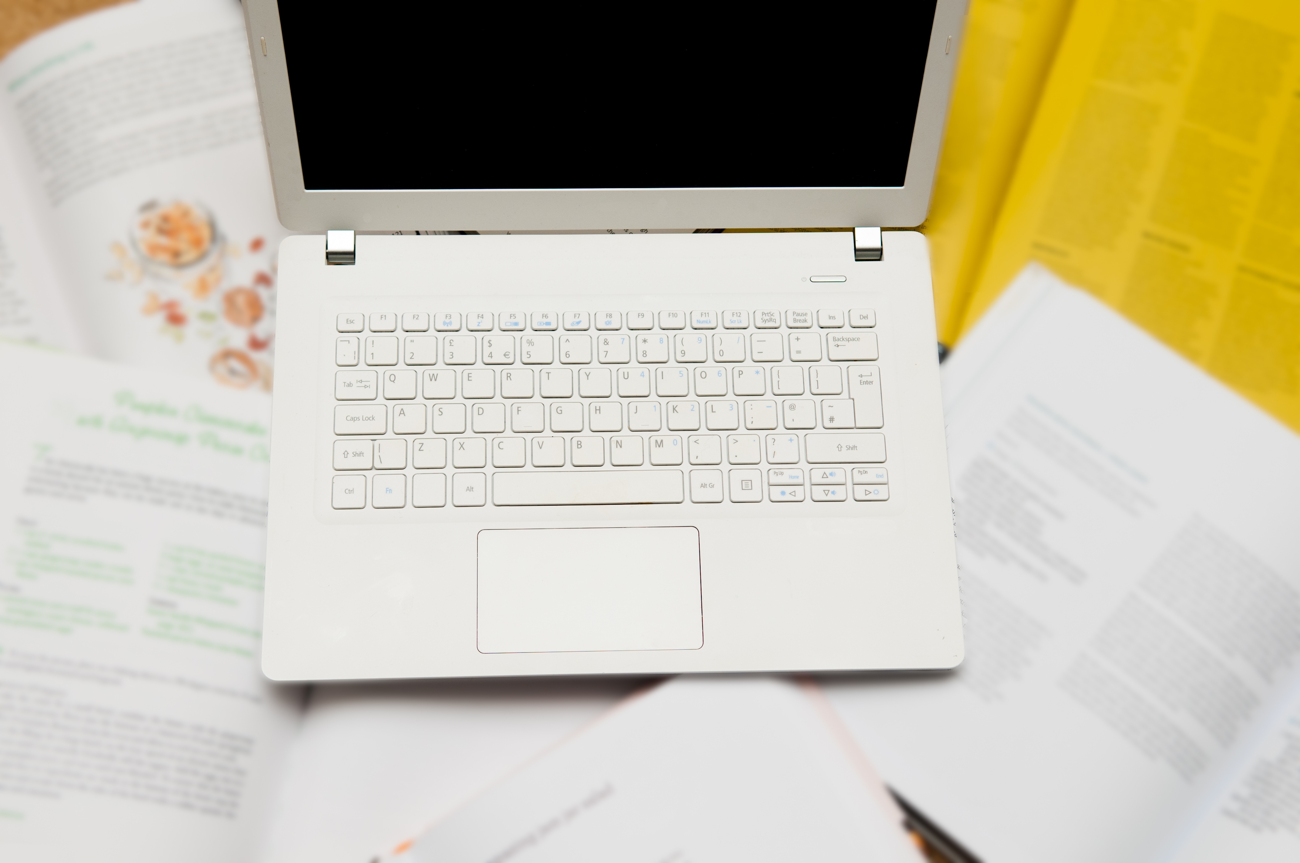Tastatur eines weißen, aufgeklappten Laptops. Daneben liegen Papiere.