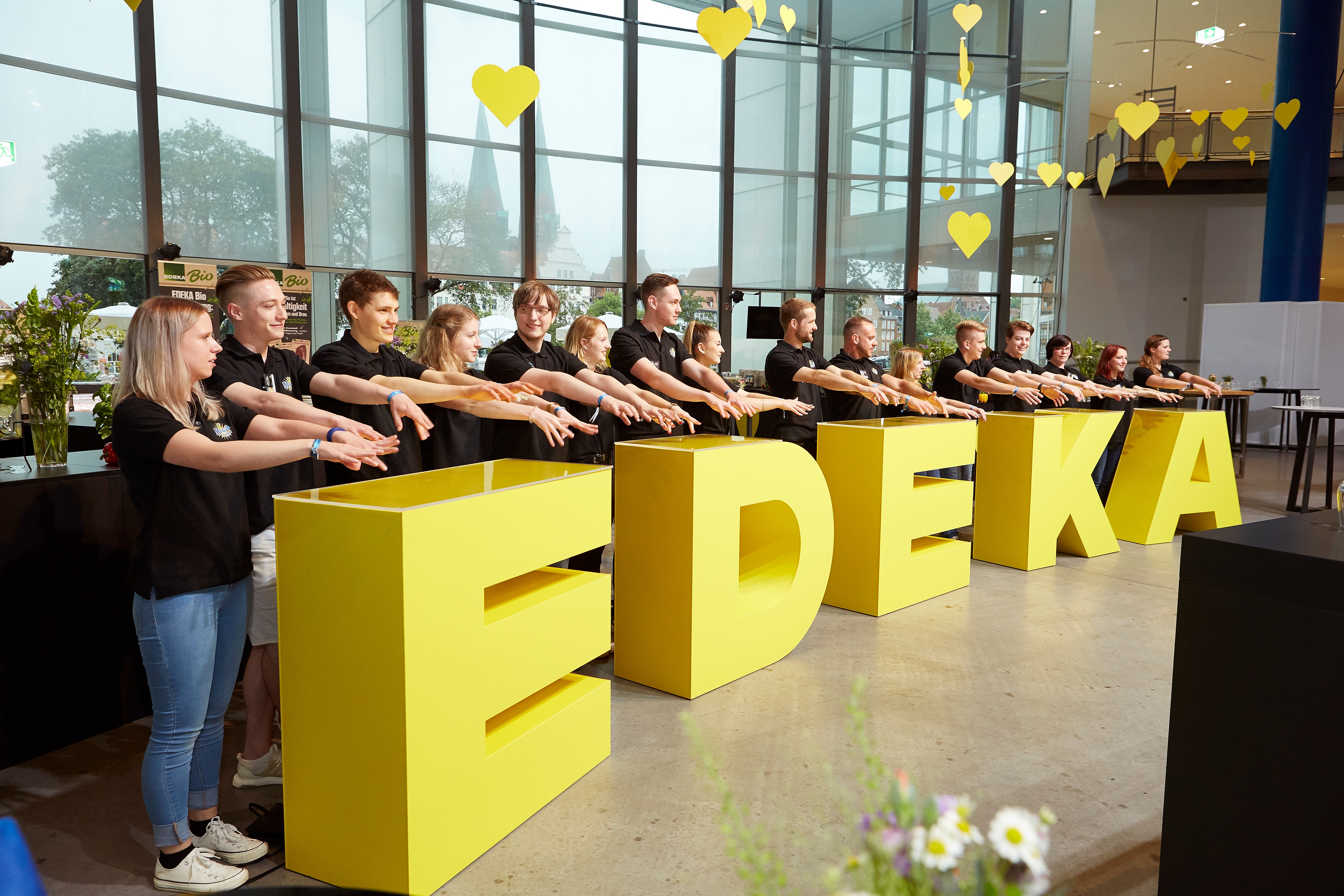 Eine Gruppe junger Menschen in schwarzen Polo-Shirts streckt die Hände nach vorne wie kurz vor einem Jubel.