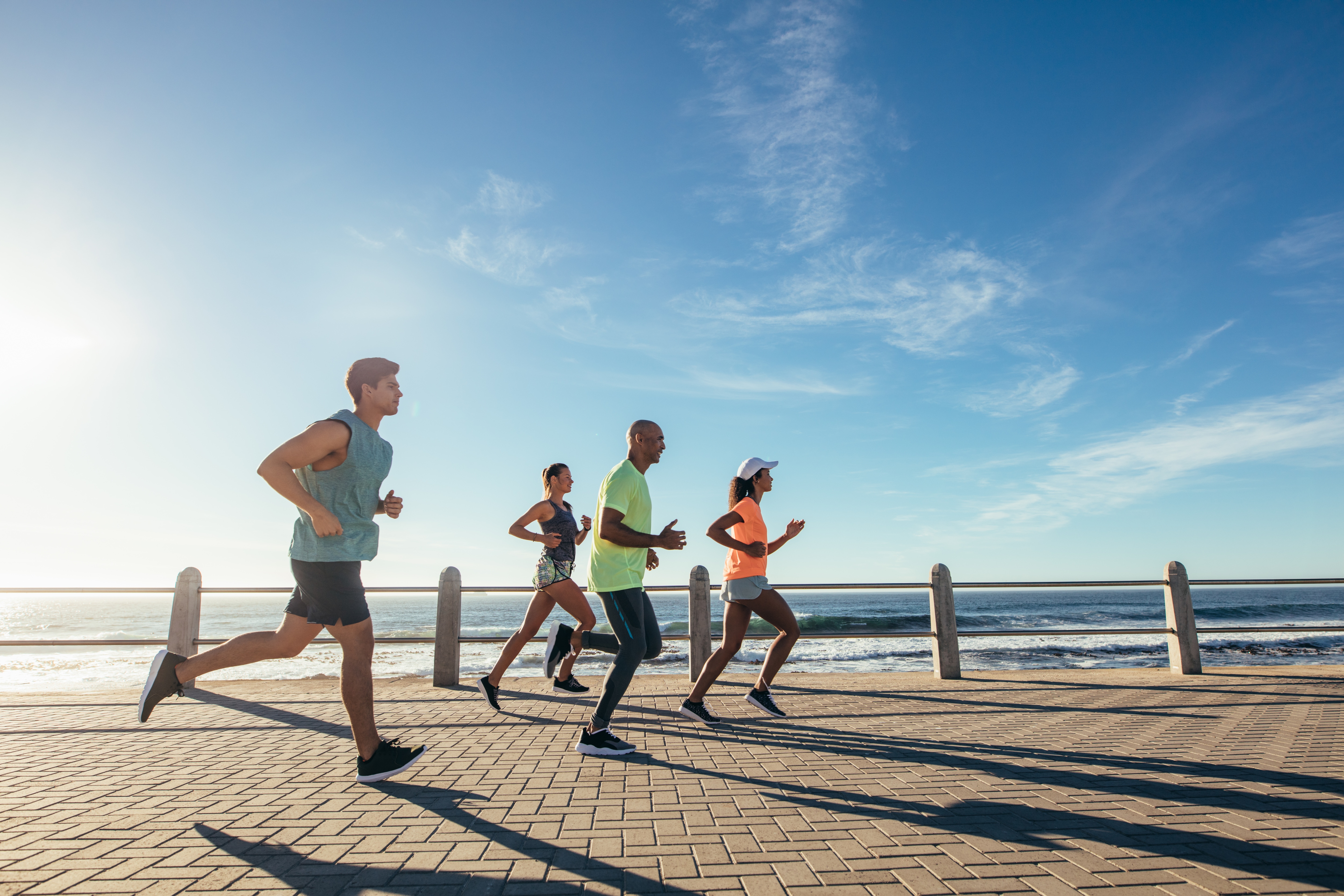 Eine Gruppe mehrerer Sportler:innen joggt entlang einer Strandpromenade.