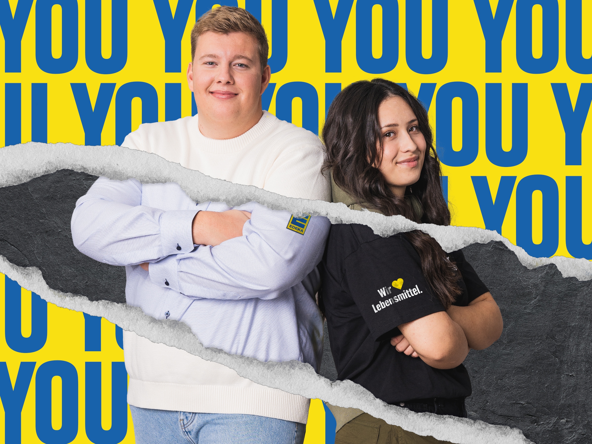 Eine junge Frau und ein junger Mann stehen vor einer Wand, auf der mit blauen Buchstaben mehrmals das Wort "you" steht