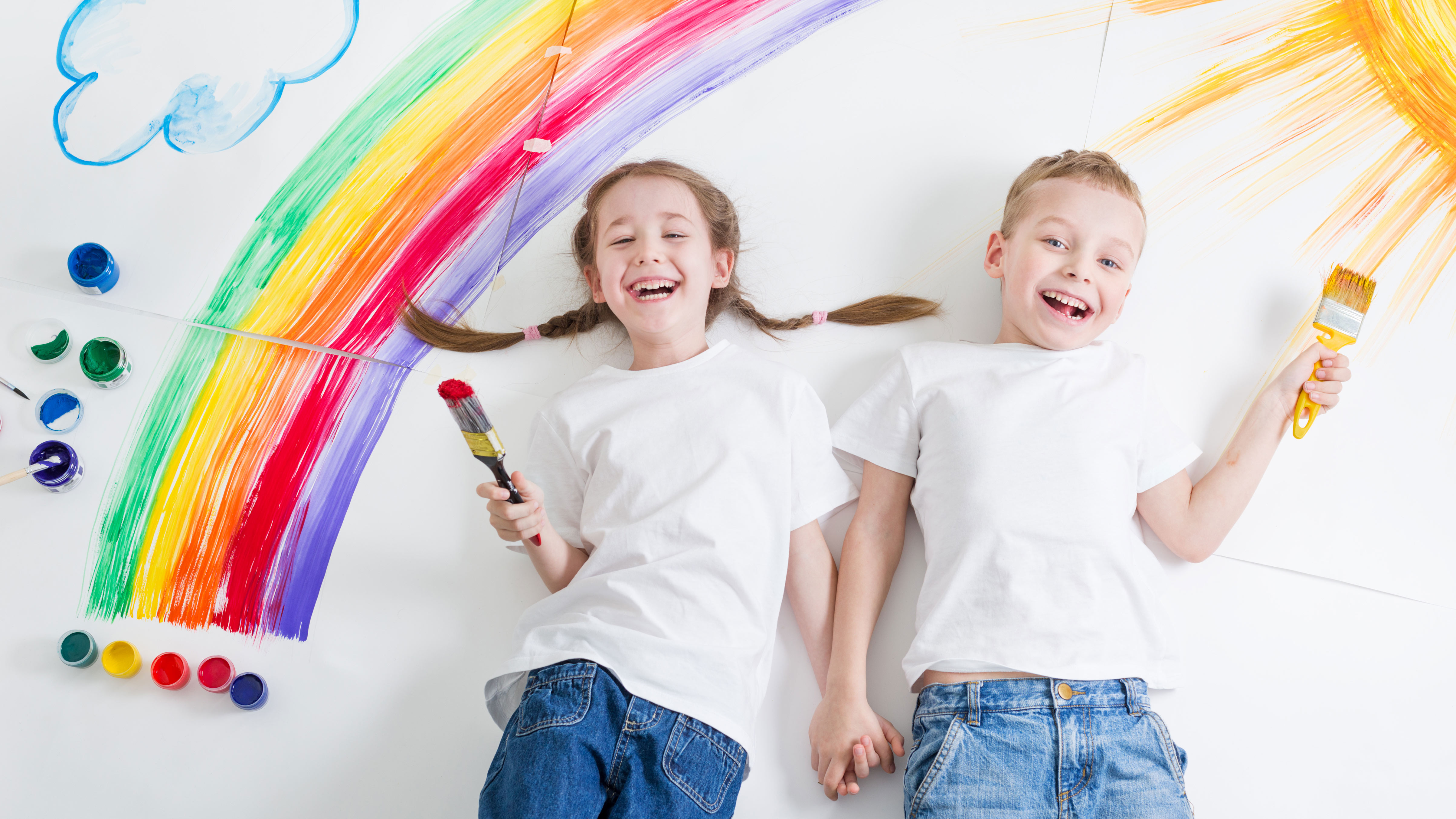 Junge und Mädchen auf Boden liegend, als Hintergrund Regenbogen & Sonne
