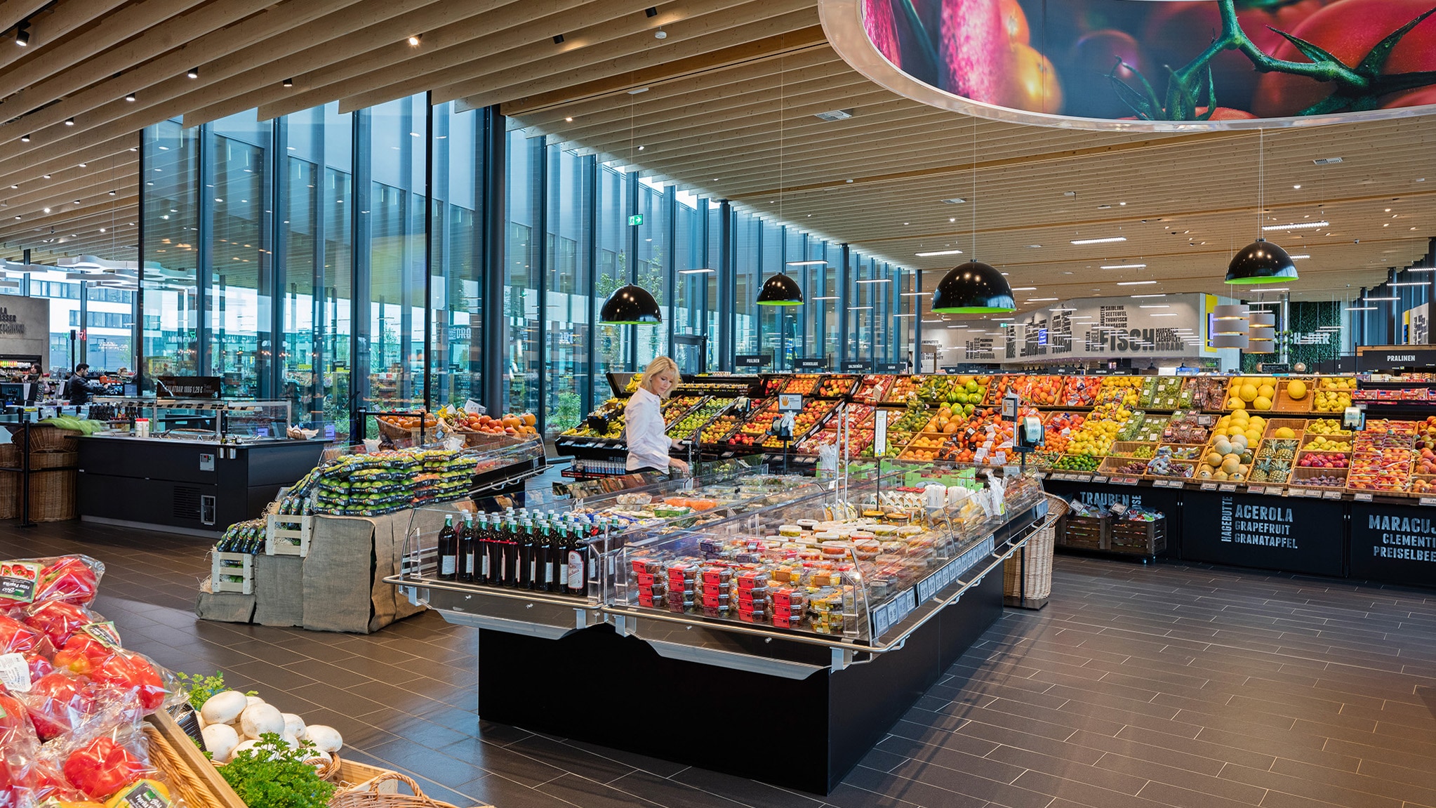 Eine Frau steht in der Obstabteilung eines EDEKA-Marktes. Die Holzdecke ist hell und alles ist gut ausgeleuchtet.