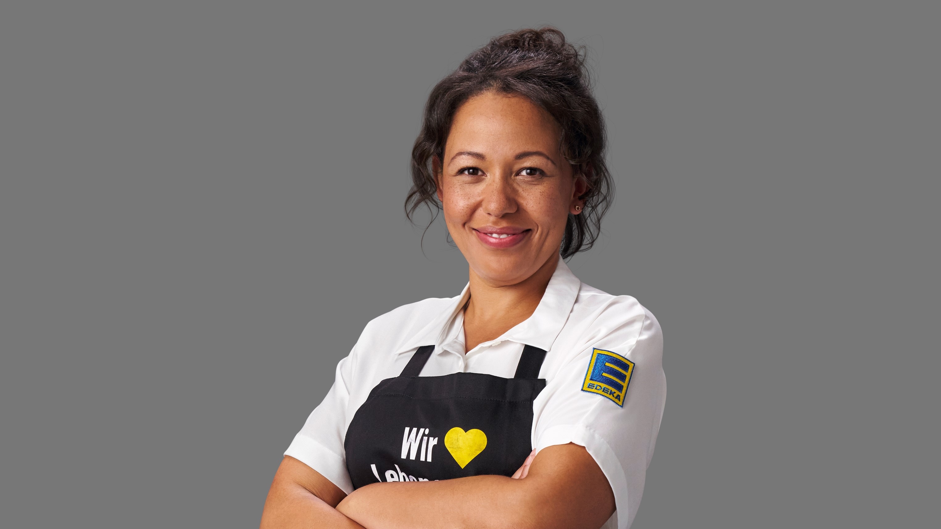 Portraitbild von Mandy Bauermeister. Sie trägt ein weißes EDEKA-Hemd und eine schwarze Schürze.
