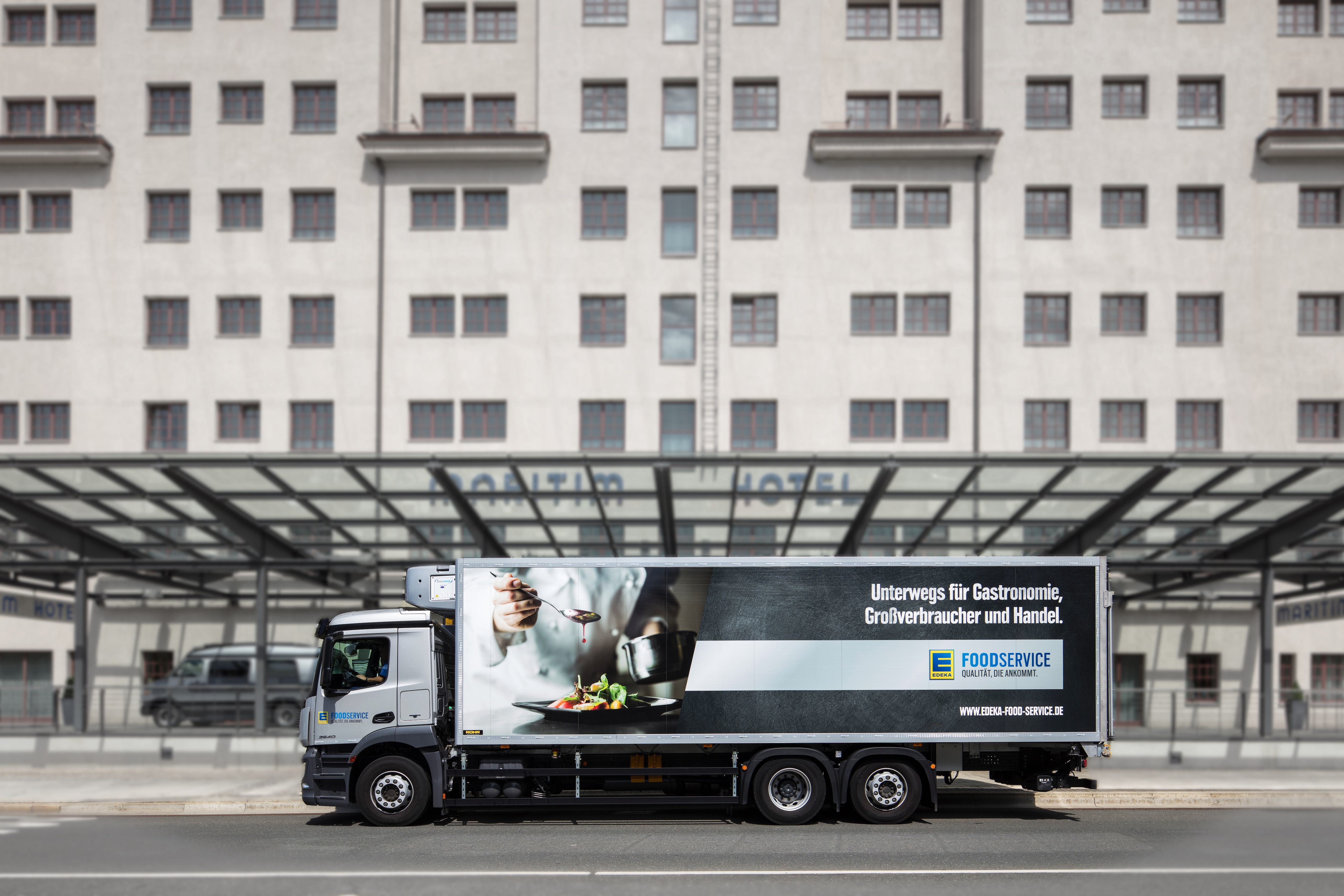 Weißer LKW von EDEKA Foodservice vor einem Hoteleingang.