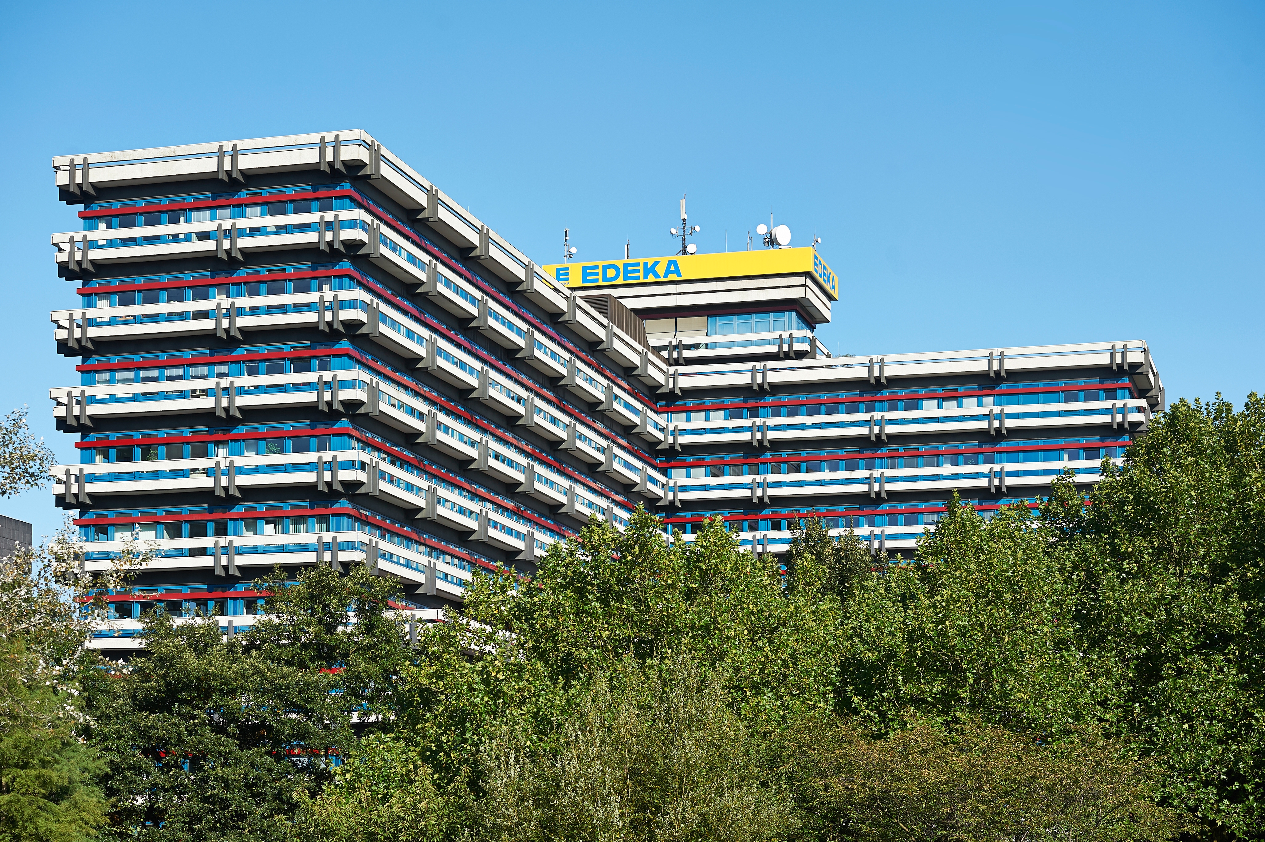 Großes Gebäude mit blauen Wänden und roten Verzierungen an den Stockwerken. An der Spitze der Fassade ist das EDEKA-Logo.