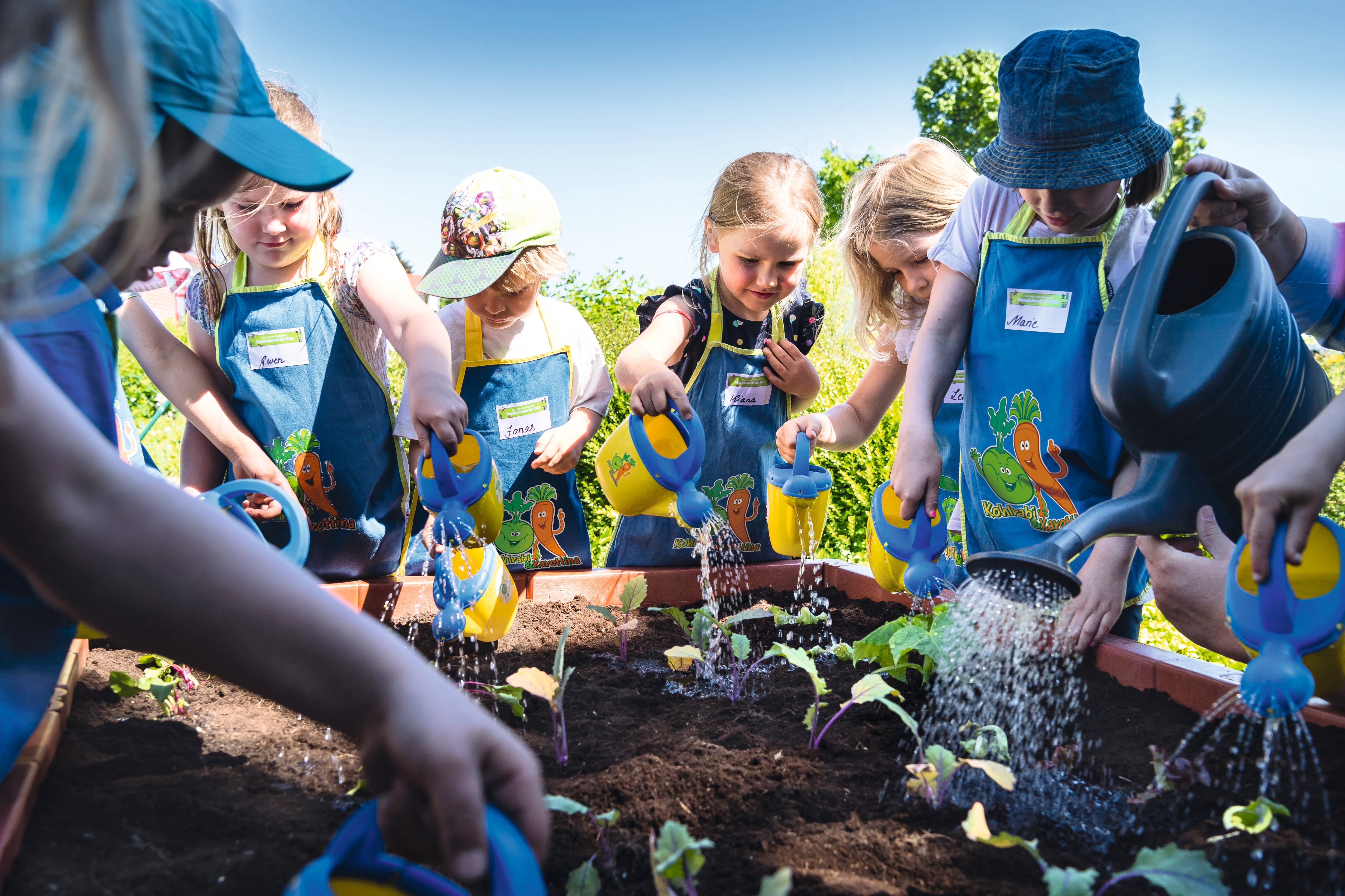 Eine Gruppe von Kita-Kindern steht an einem Hochbeet, das mit Erde und Setzlingen gefüllt ist.