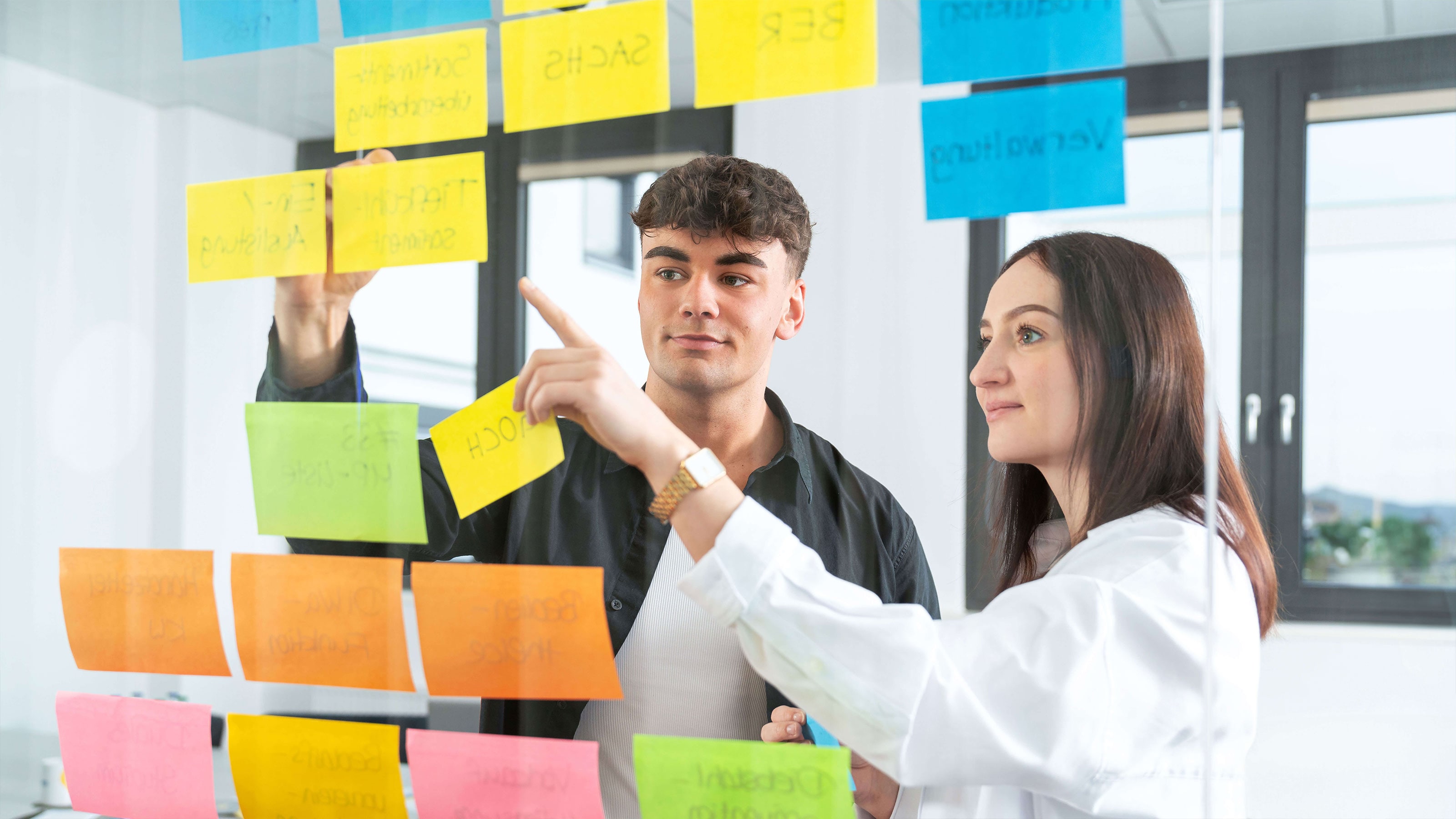Zwei Studierende arbeiten mit gelben Post-its an einem Projekt