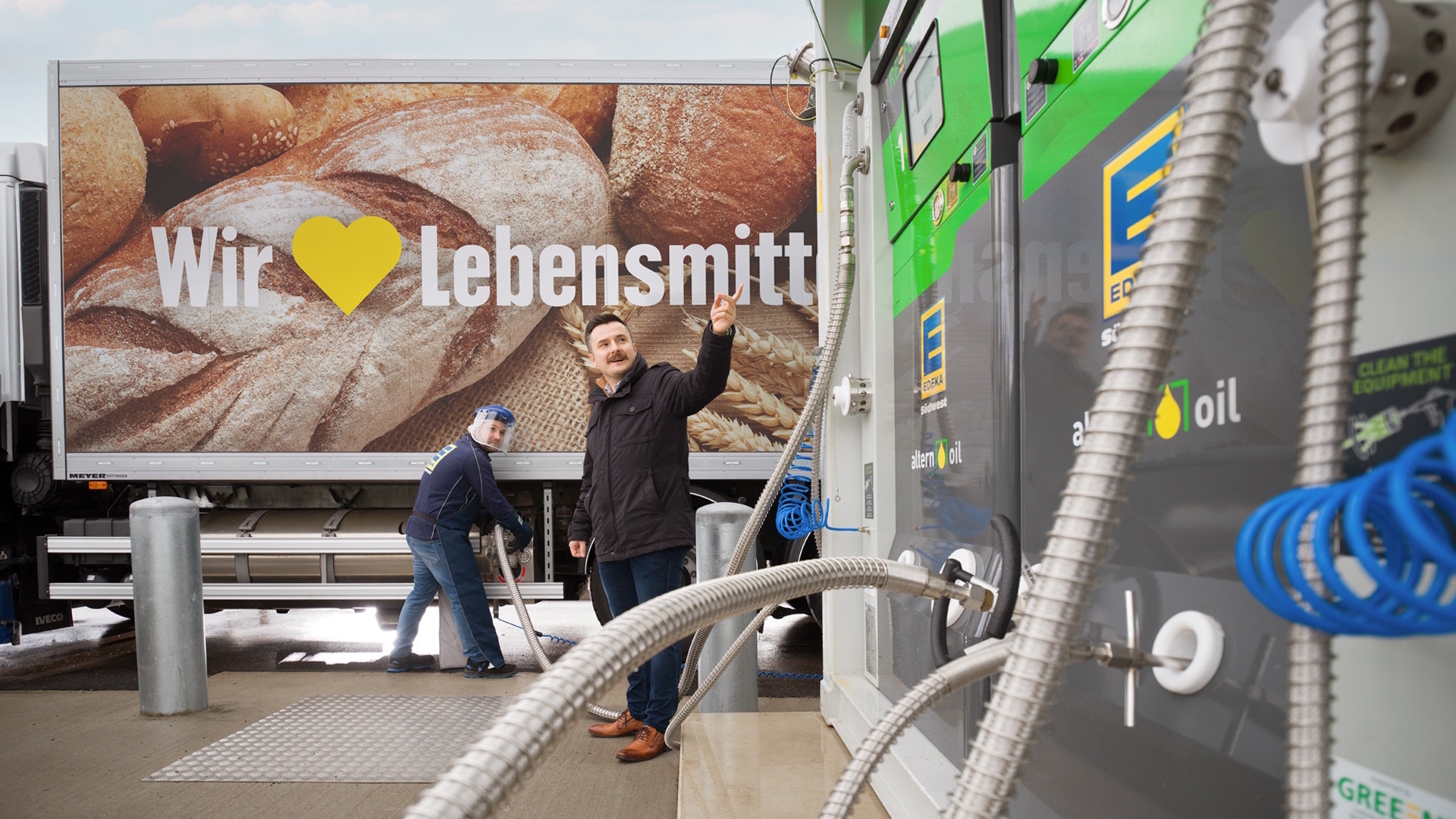 Ein Lkw mit der Aufschrift "Wir ♥ Lebensmittel" wird von einem Mann an der LNG-Tankstelle bedankt, ein zweiter steht daneben