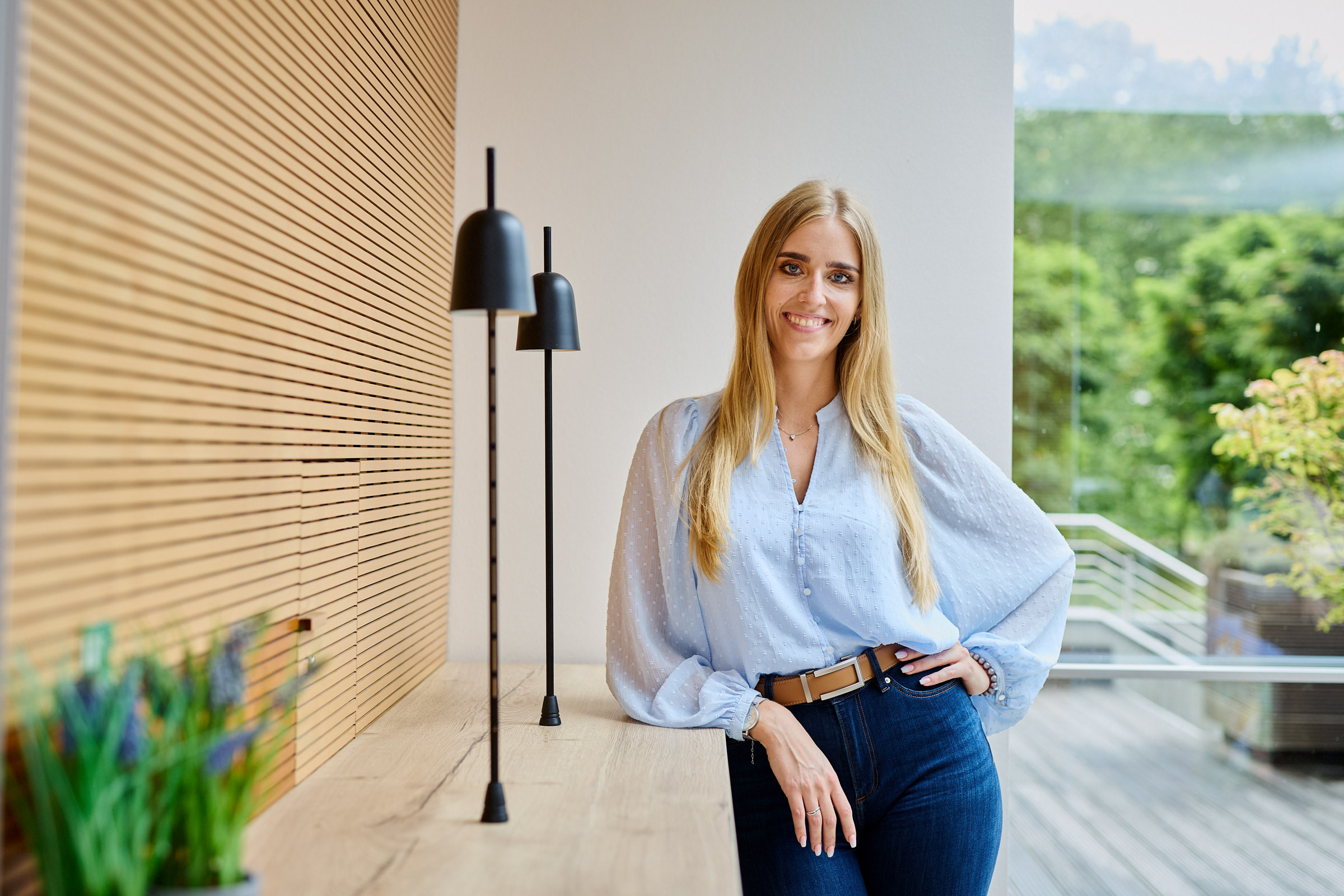 Leandra Thielemann lehnt an einer hellen Holzwand und lächelt in die Kamera.