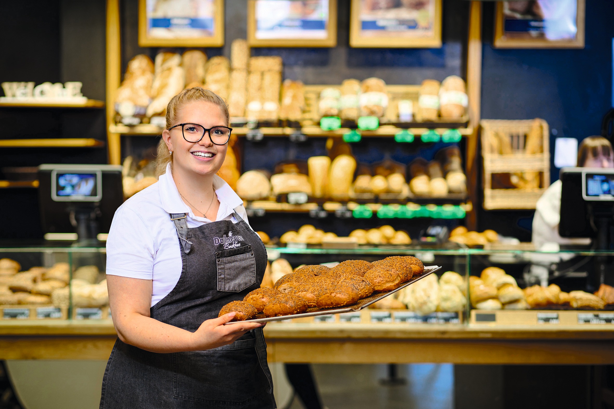 Eine Bäckereifachverkäuferin präsentiert frisch gebackene Brötchen auf einem Backblech