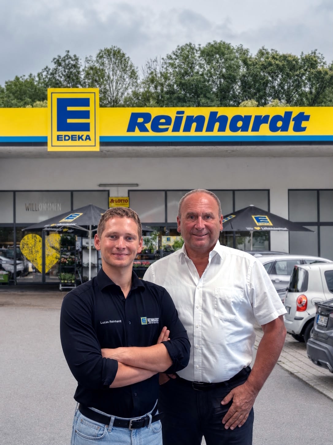 Ein junger Mann mit schwarzem Hemd und sein Vater stehen stolz und mit einem Lächeln vor dem EDEKA Markt Reinhardt