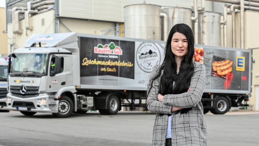 Eine junge Frau mit langen schwarzen Haaren steht vor einem LKW von BauernGut. 