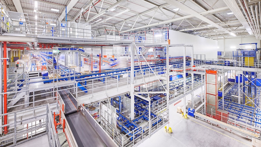 hell beleuchtetes Logistikzentrum mit mehreren Ebenen von Förderbändern und automatisierten Sortieranlagen.