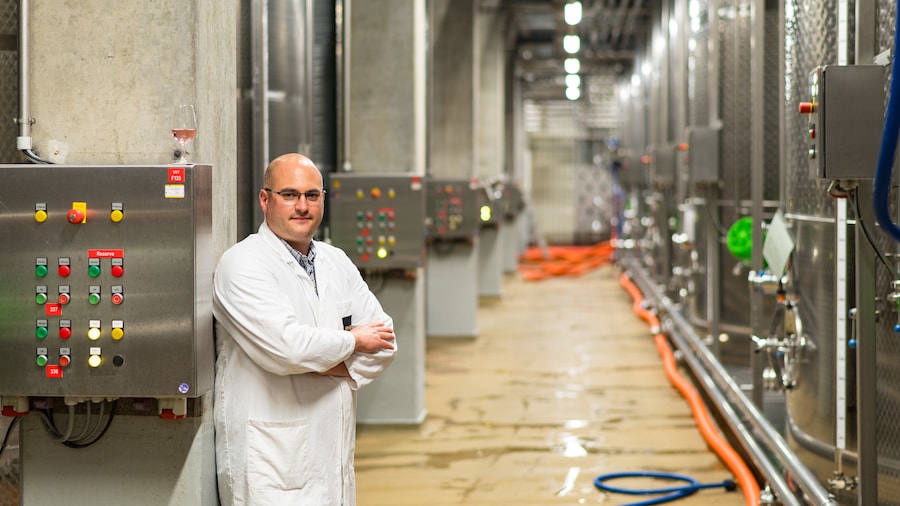 Ein Mitarbeiter im Kittel steht mit verschränkten Armen vor einer Abfüllanlage