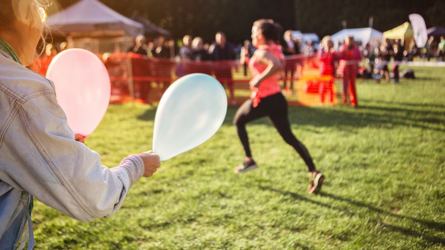 Eine laufende Frau wird mit Luftballons angefeuert. 