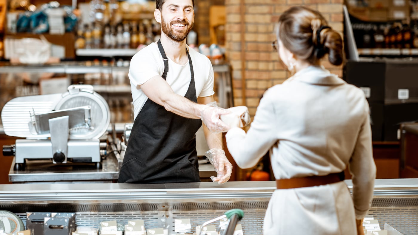Mitarbeiter der Bedientheke überreicht einer Kundin Ware
