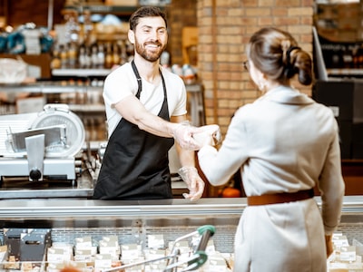 Mitarbeiter der Bedientheke überreicht einer Kundin Ware
