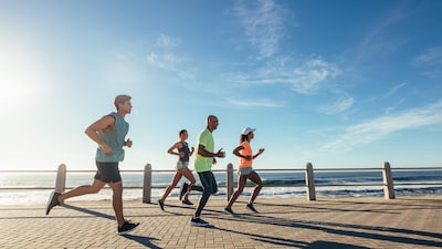 Eine Gruppe mehrerer Sportler:innen joggt entlang einer Strandpromenade.
